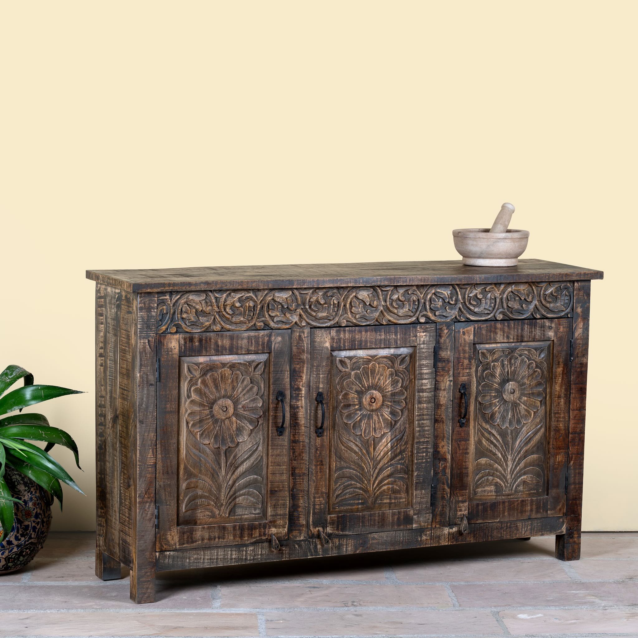 Side angle image of a dark brown hand carved mango wood sideboard with floral design and ample storage.