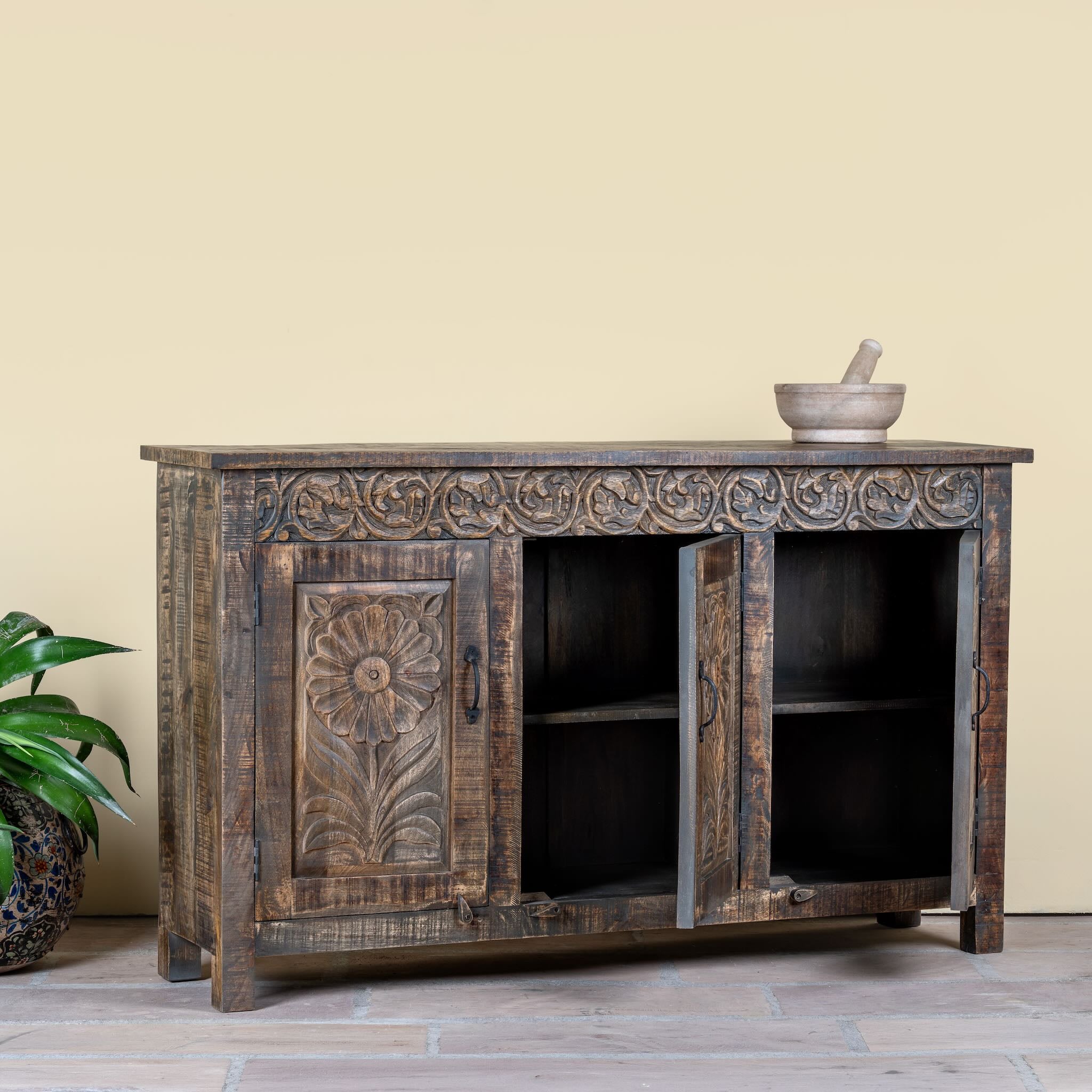 Side angle image with open doors of a dark brown hand carved mango wood sideboard with floral design and ample storage.