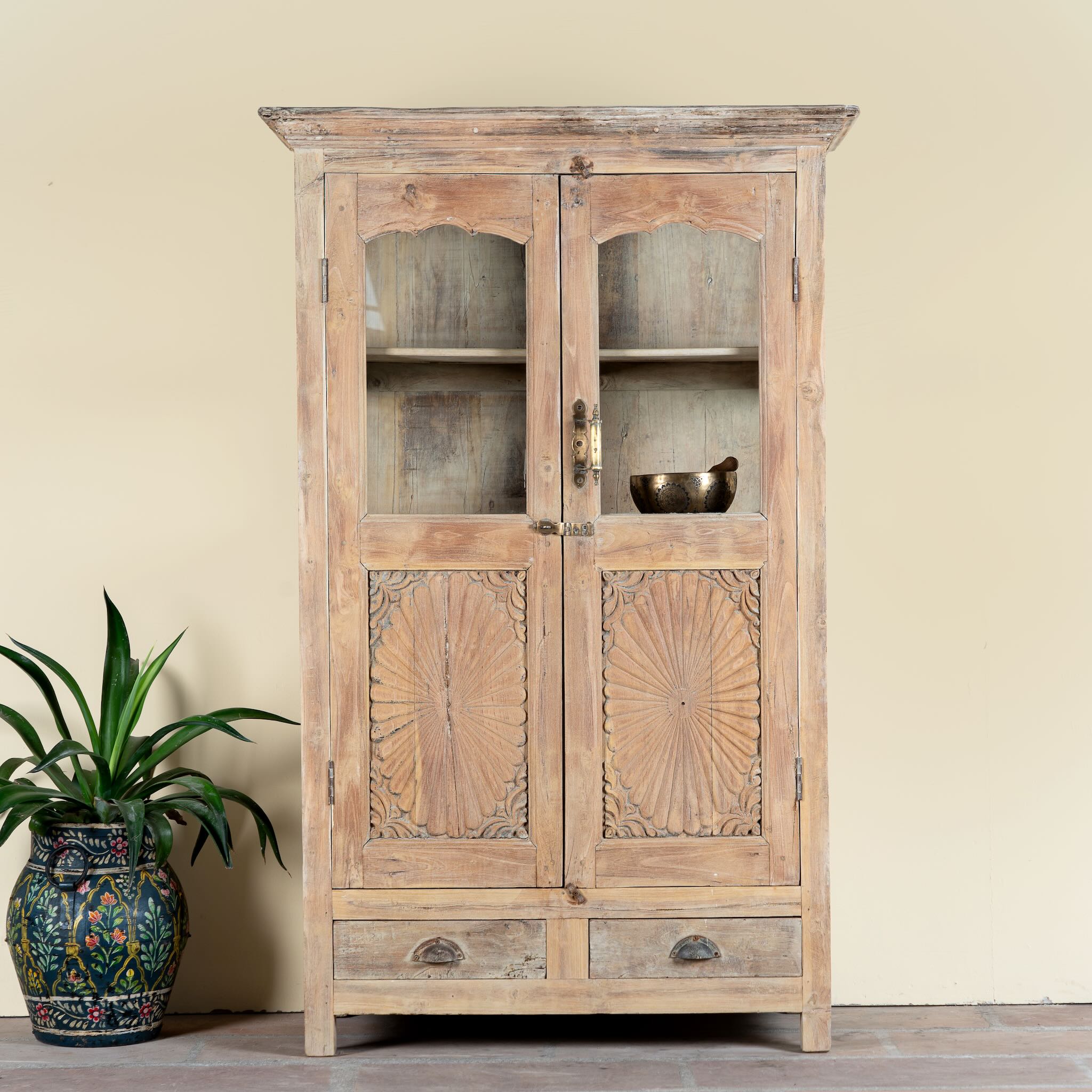 Reclaimed teak wood showcase Aasta with Mediterranean design, featuring hand-carved doors, glass panels, and drawers. A unique piece of refurbished Indian furniture offering elegant display and practical storage.