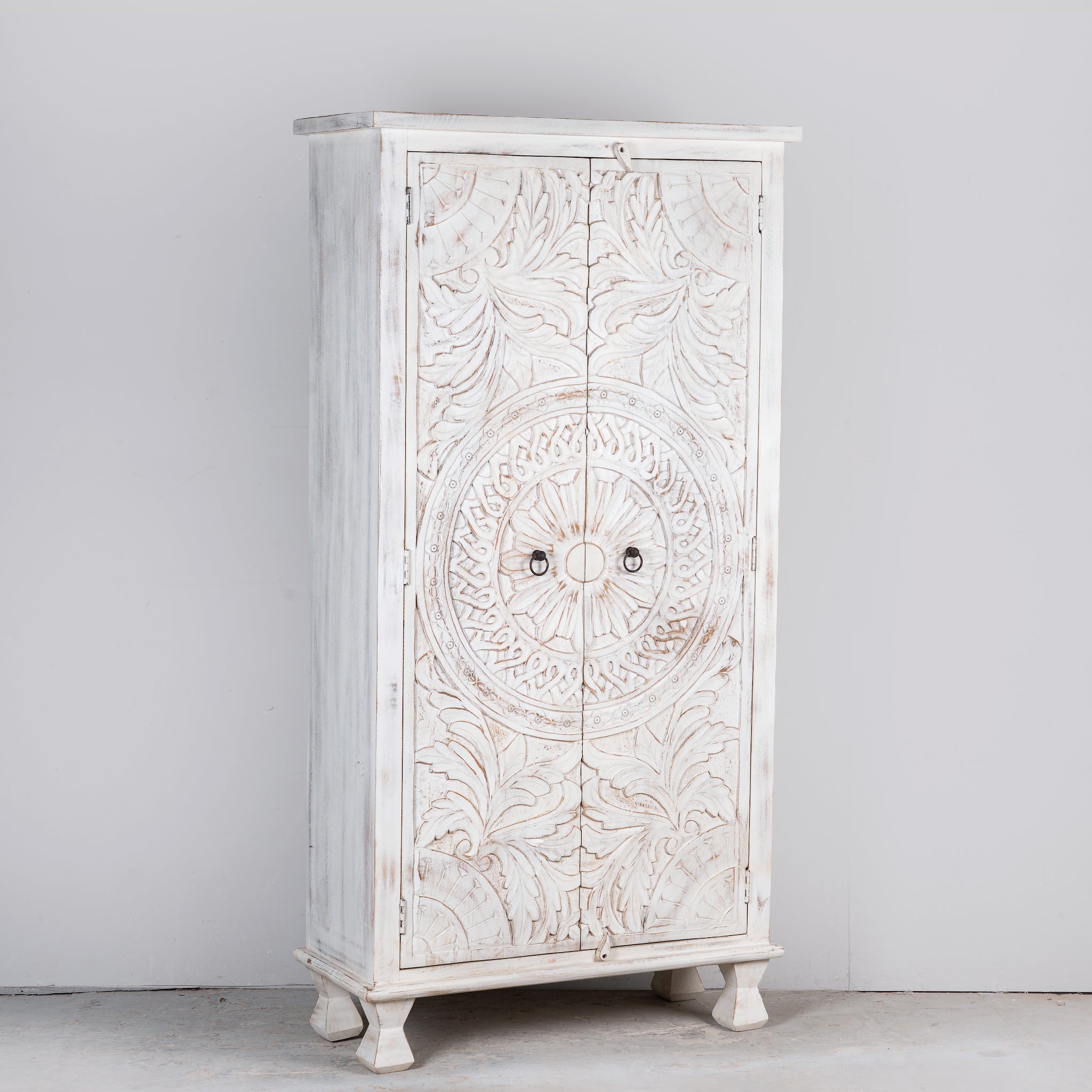 Side angle image of an Aila handcrafted solid mango wood wardrobe with intricately hand-carved Indian doors, four spacious storage compartments, natural wood grain, and Mediterranean-inspired design, 180cm.