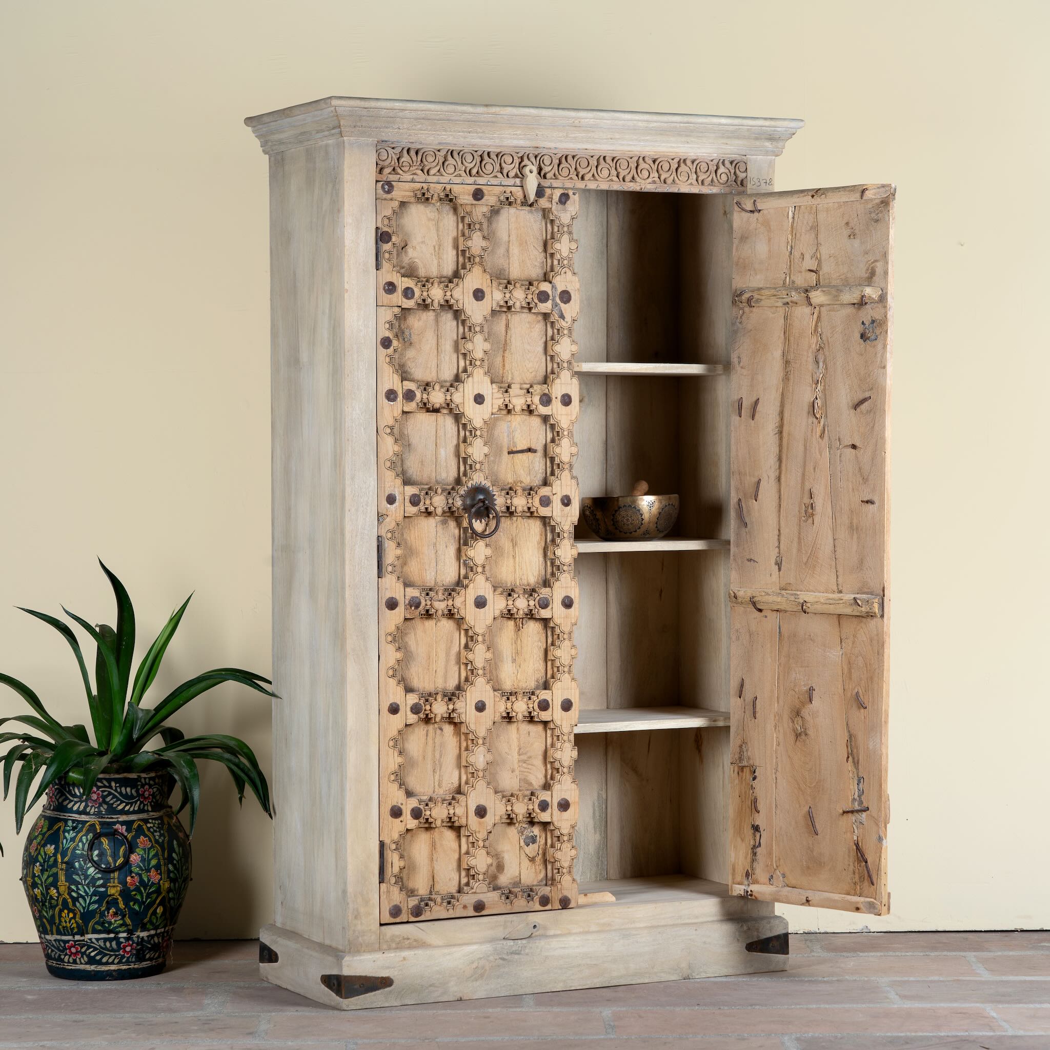 Side angle image with open doors of a reclaimed wood wardrobe Akhila featuring an old Indian door front with carved details and iron hardware. A sustainable furniture piece and unique old door cabinet for soulful, heritage-inspired interiors.