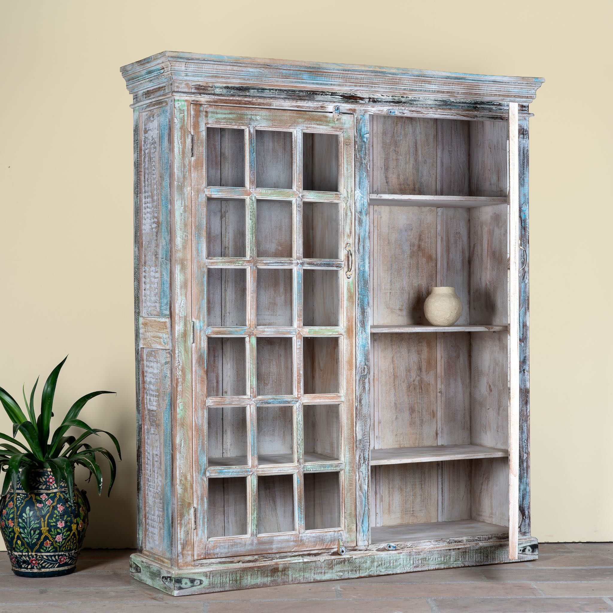 Side angle image with open door of a reclaimed wood display cabinet Amara with distressed turquoise finish and glass-panelled doors. Sustainable living room furniture and vintage furniture piece with spacious shelving and authentic patina.