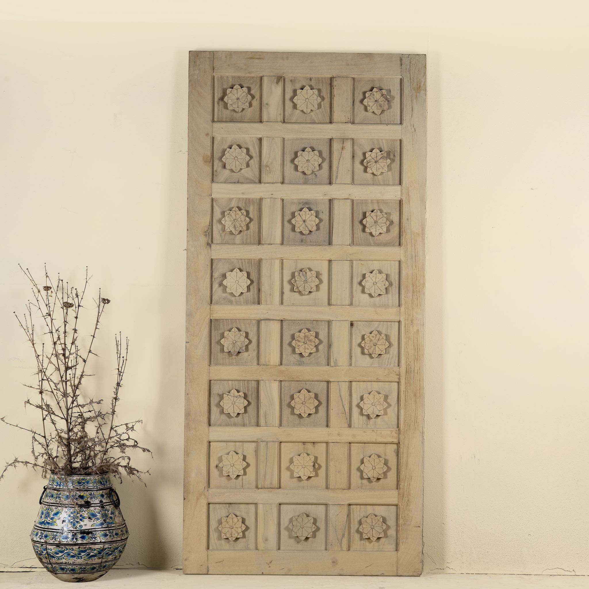 Hand-carved sliding door panel made from reclaimed wood, featuring symmetrical floral motifs in square reliefs for a warm, artisanal statement piece.