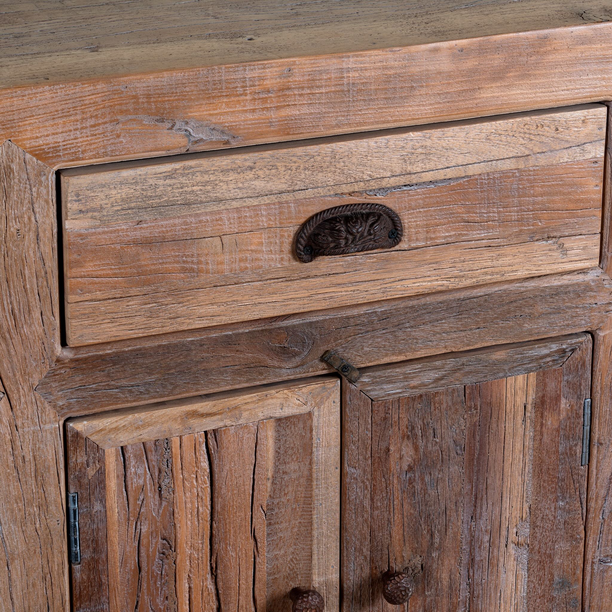 Close up image of a reclaimed wood sideboard Amira in a rustic minimalist design, featuring three drawers and six doors with iron handles. A sustainable piece of living room furniture with natural textures and timeless appeal.