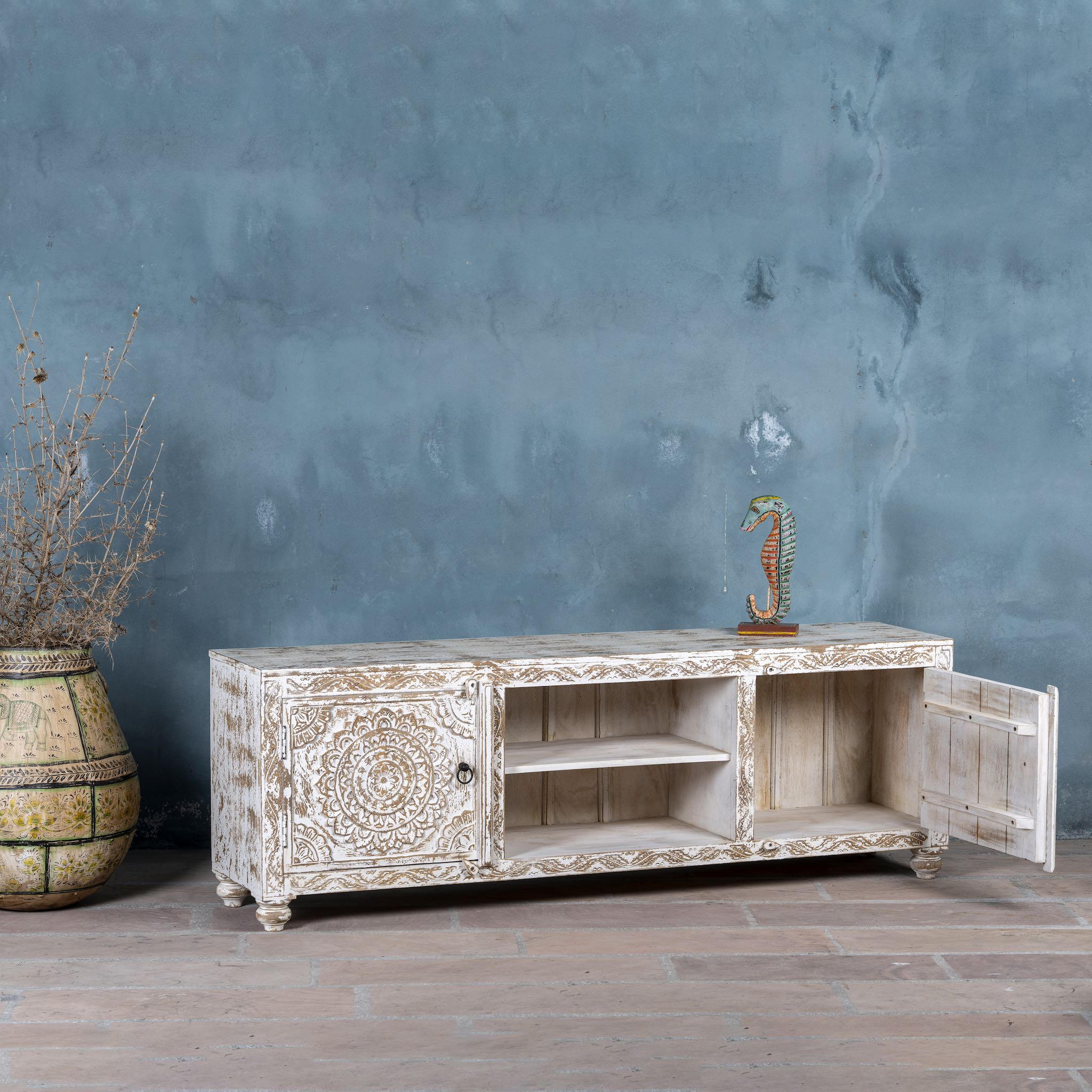 Open door image of a white washed mango wood lowboard with carved floral doors and open shelving, 180 × 40 × 60 cm.