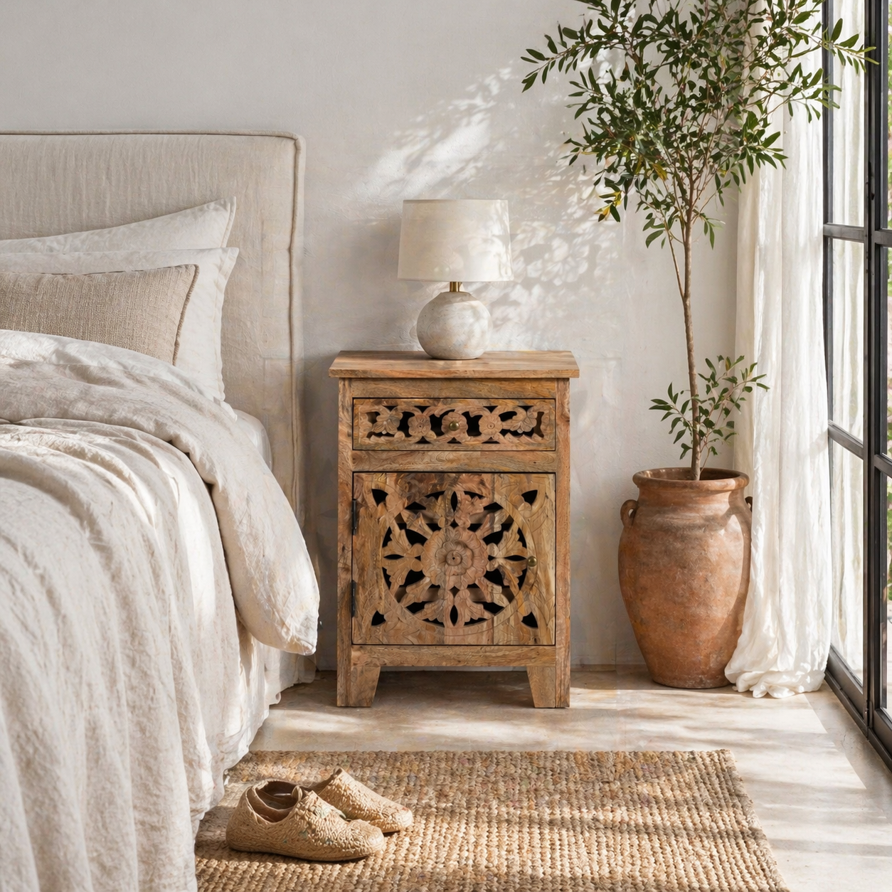 Lifestyle scene with a mango wood bedside table with floral and geometric carvings; natural finish mango wood furniture ideal for bedroom furniture, 45 × 65 × 35 cm.