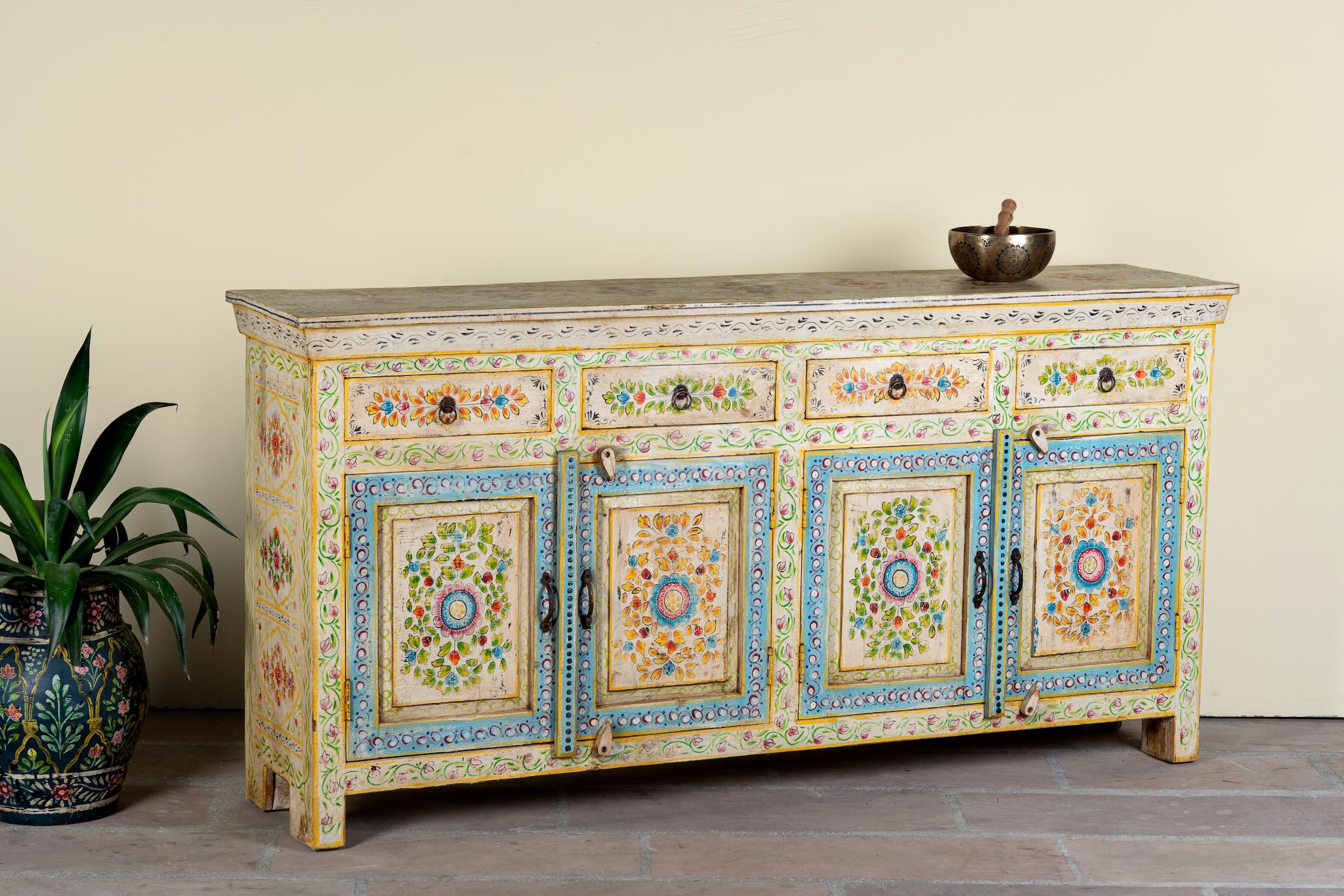 Side angle image of a hand-painted reclaimed wood cabinet Anwita in Mediterranean Boho style with floral motifs, four drawers, and four doors. A colourful and sustainable statement piece for boho chic living room décor.