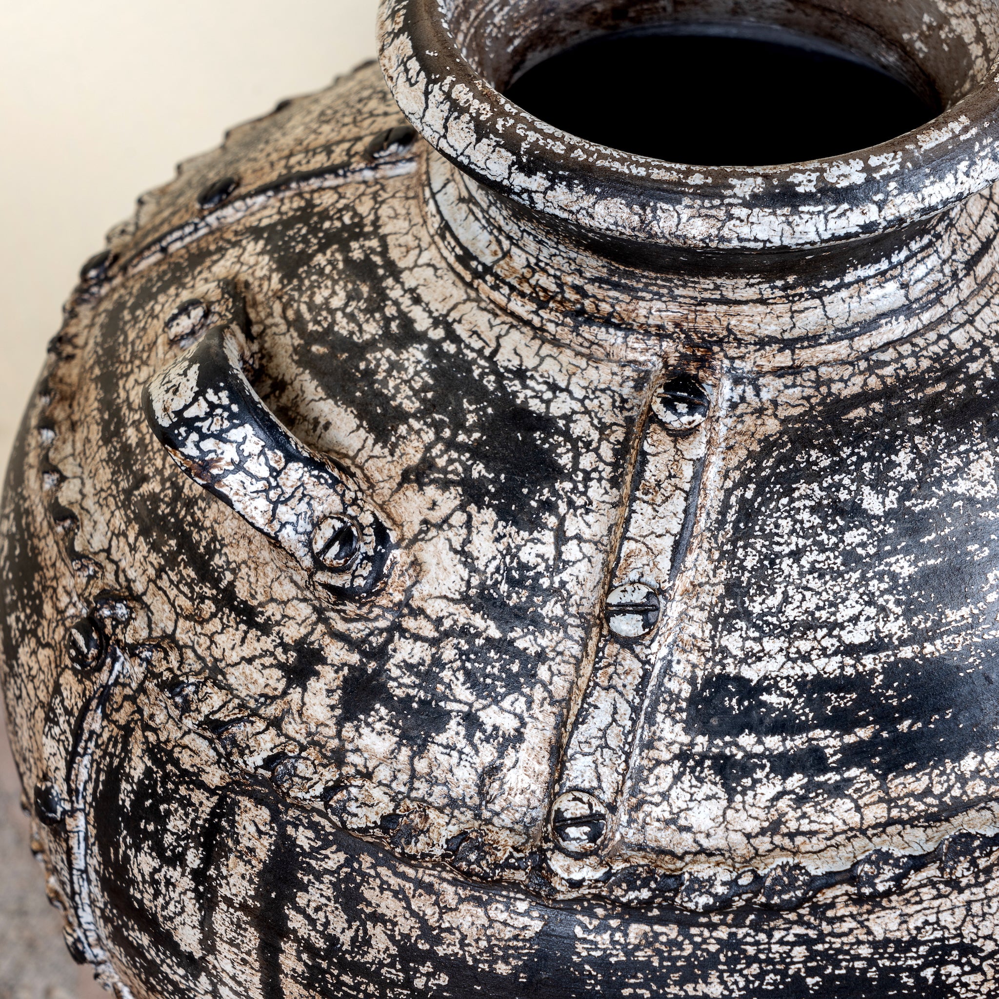 Close up image of a hand-painted clay vase with vintage distressed charcoal finish, sculptural side handles and decorative rivet details, 30x38cm.