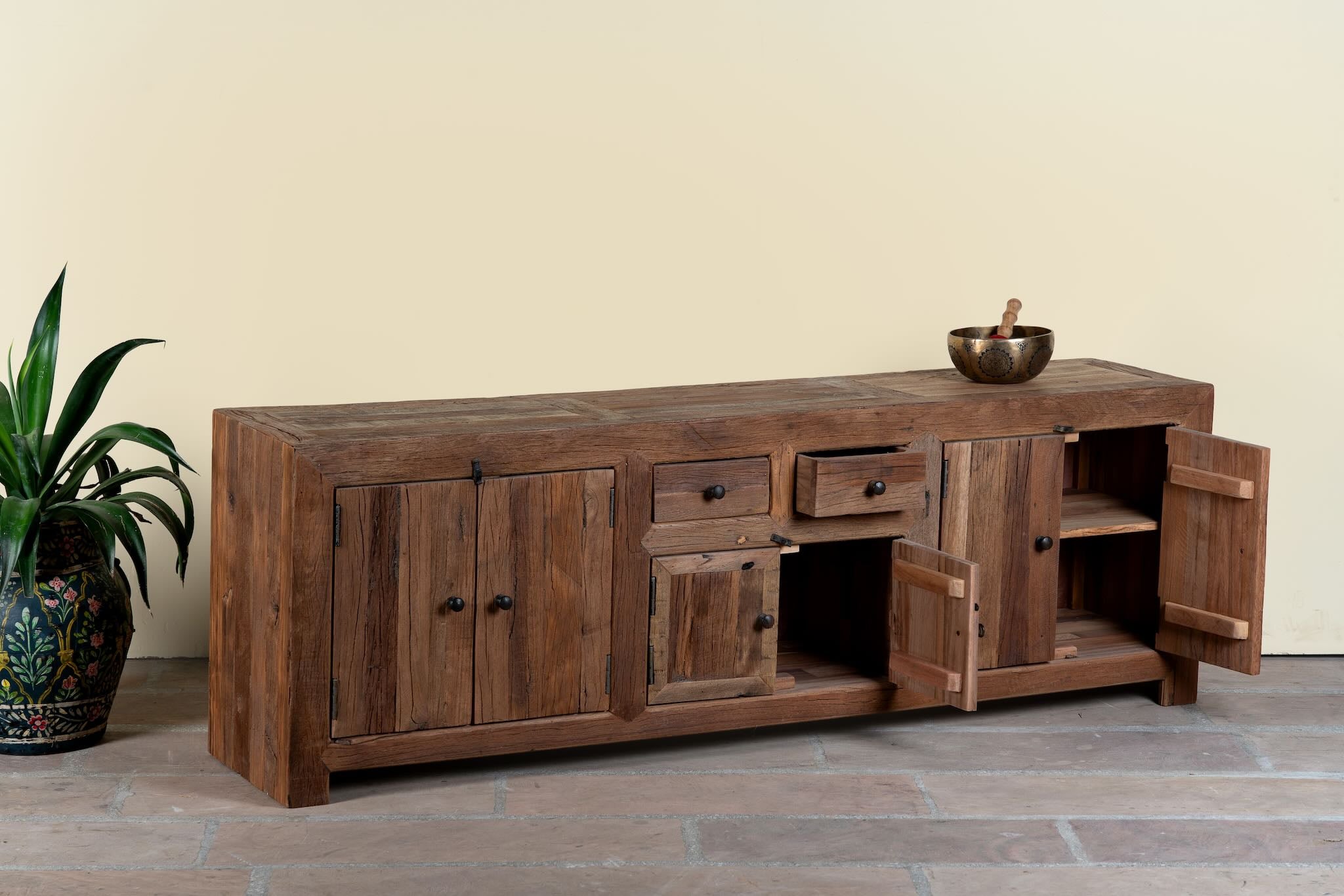Wooden sideboard Ariana with open doors in a room with a plant and light-colored wall.