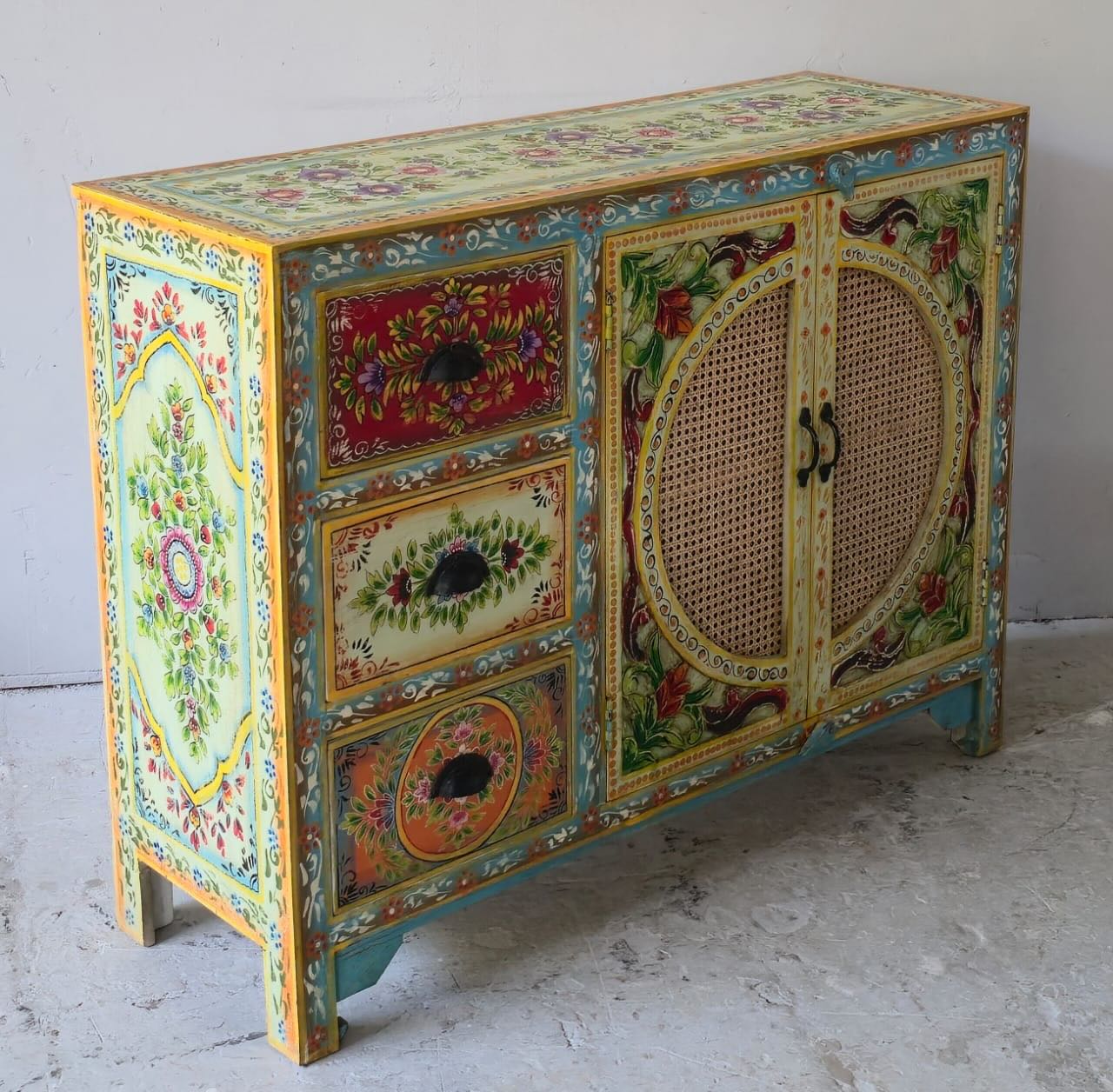 Side angle image of a hand painted sideboard Ashara made of mango wood with rattan inserts; Ibiza-inspired boho chic furniture, 120 × 40 × 92 cm.