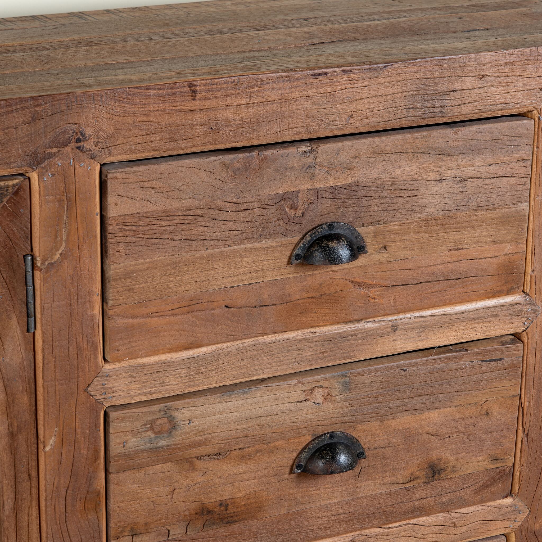 Close up image of a reclaimed wood sideboard Avika in a rustic minimalistic design with three drawers and two double-door cabinets. A sustainable furniture piece with warm wood tones and black iron handles, perfect for eco-conscious interiors.