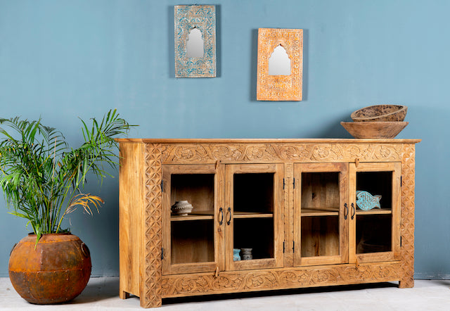 Side angle image of a hand-carved wooden showcase Barot made from natural mango wood, featuring detailed floral carvings across its front. A sustainable piece of Indian furniture online ideal for living room furniture with a Mediterranean and boho-style design.