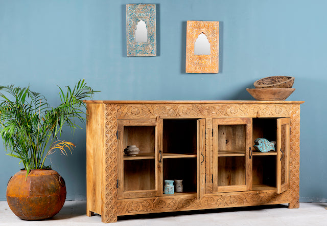 Side angle image with open door of a hand-carved wooden showcase Barot made from natural mango wood, featuring detailed floral carvings across its front. A sustainable piece of Indian furniture online ideal for living room furniture with a Mediterranean and boho-style design.