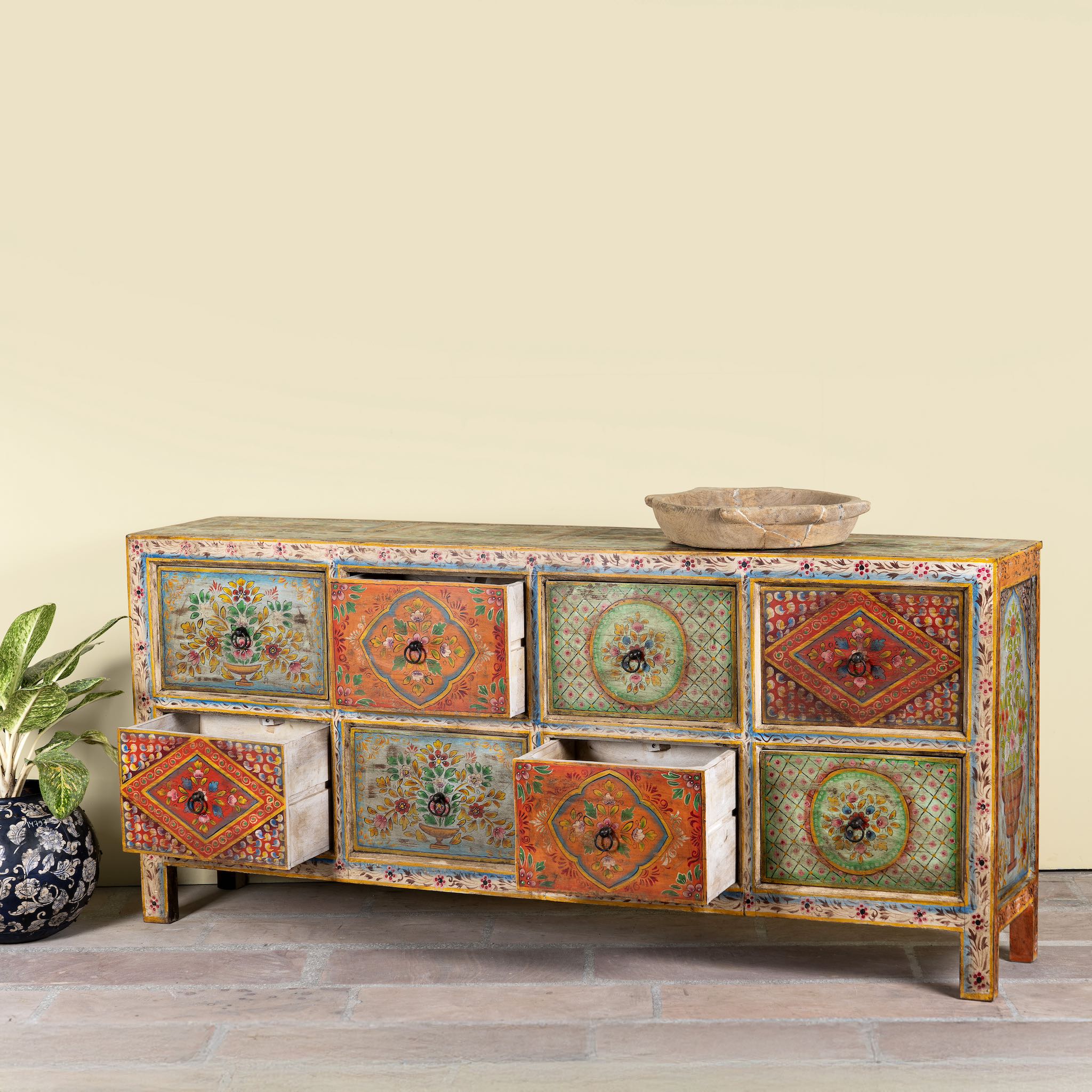 Side angle image with open drawers of a hand painted sideboard with 8 drawers made of natural mango wood; artisanal chest for bohemian interior, 200 × 40 × 90 cm.
