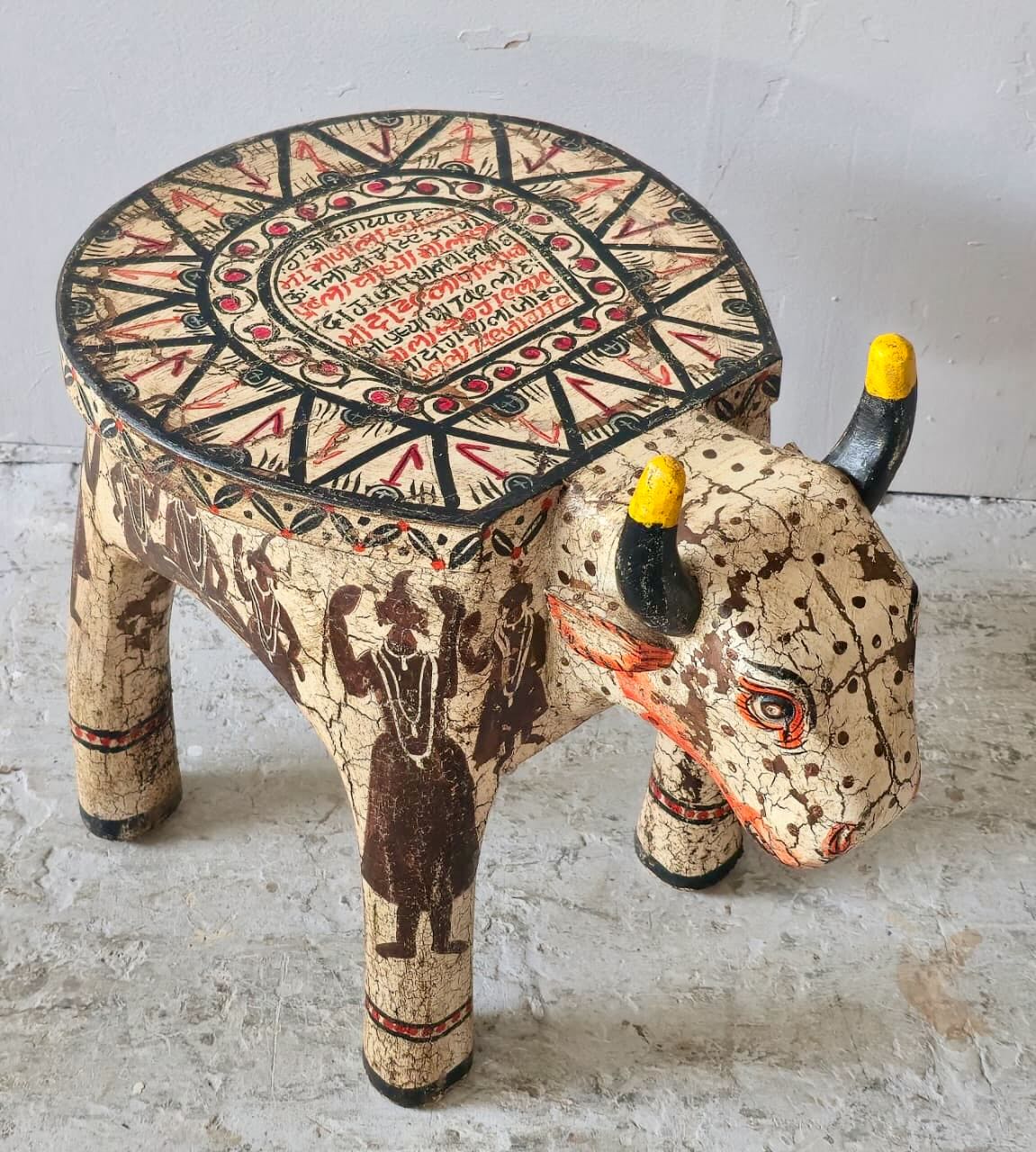 Hand-painted wooden cow-shaped side table with Indian script and blue folk art patterns, perfect for vintage and India-inspired home interiors.