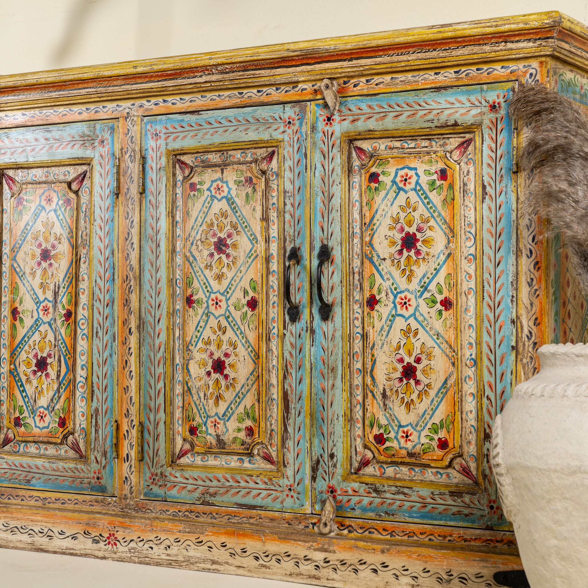 Side angle image of a hand painted wooden dresser with floral and geometric motifs, reclaimed wood living room furniture in vintage boho style, 170 × 45 × 95 cm.