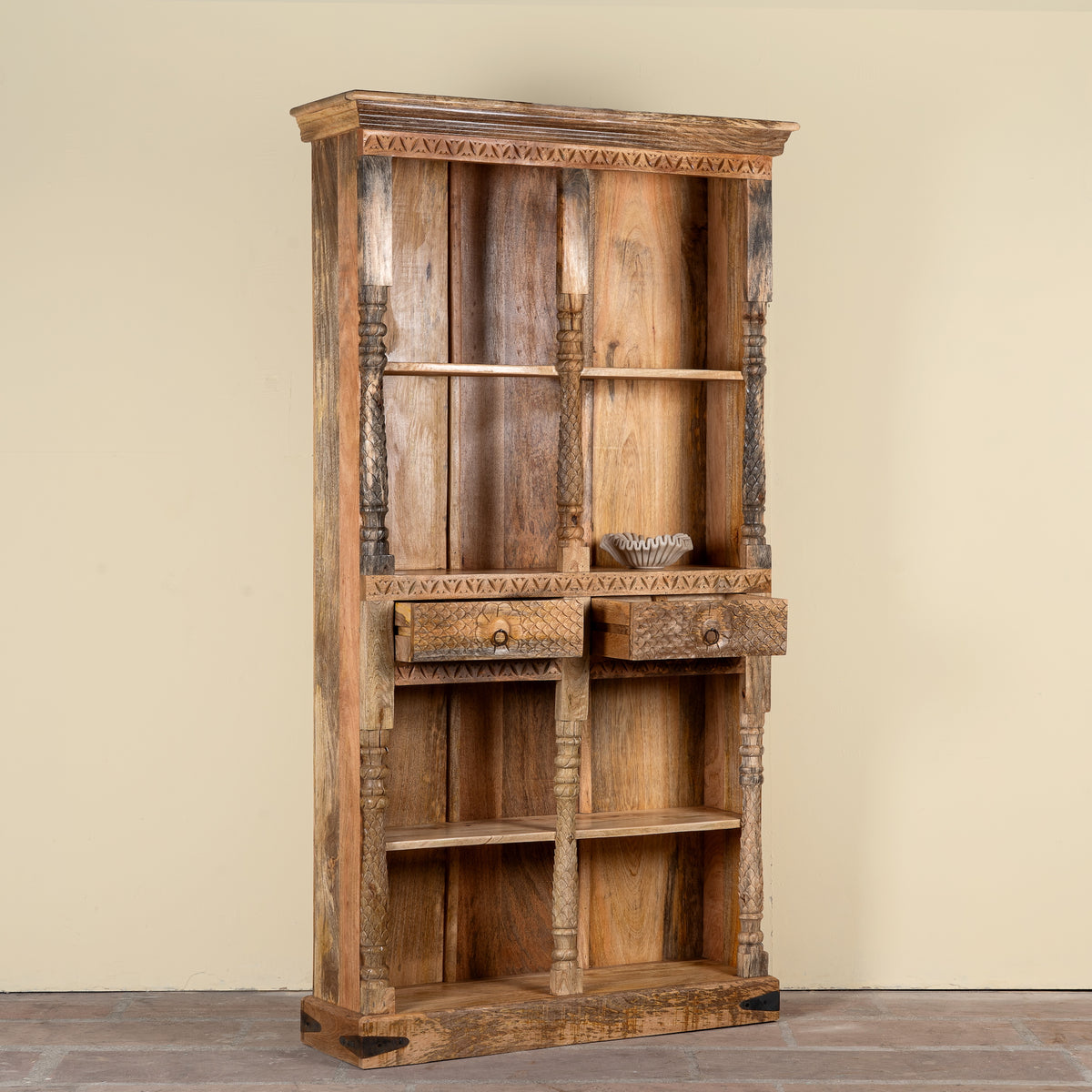 Side angle image with open helf of a handcrafted mango wood bookshelf with carved detailing – mango wood shelving and carved wooden furniture in a warm brown finish for timeless interiors.