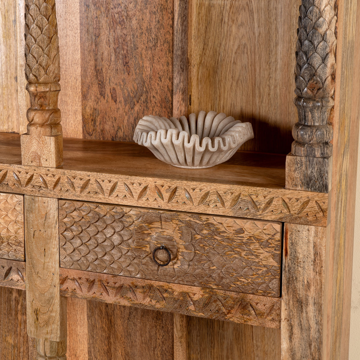 Close up image of a handcrafted mango wood bookshelf with carved detailing – mango wood shelving and carved wooden furniture in a warm brown finish for timeless interiors.