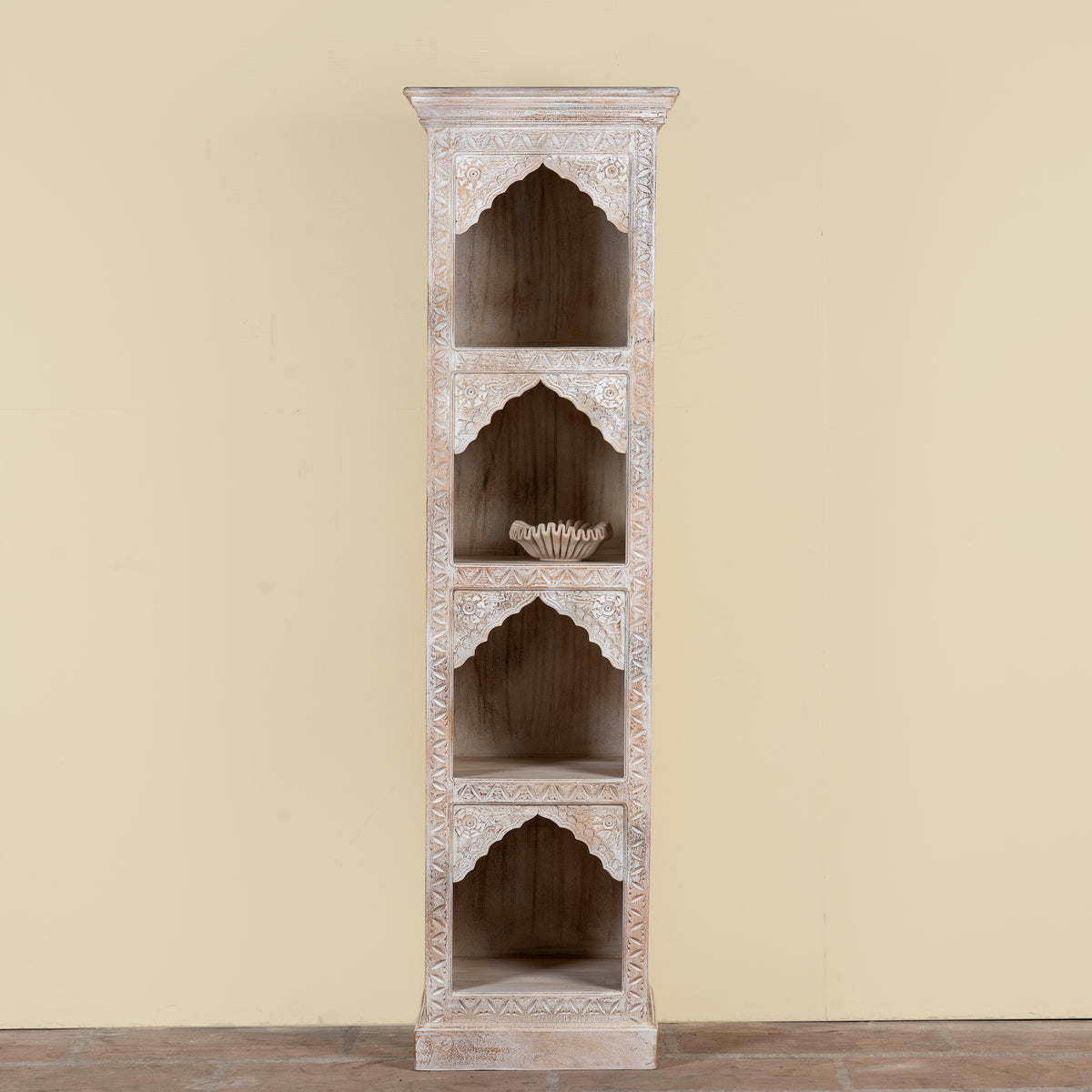 A tall, narrow wooden shelving cabinet with four arched recessed shelves, featuring distressed white and light gray painted detailing on a beige background.