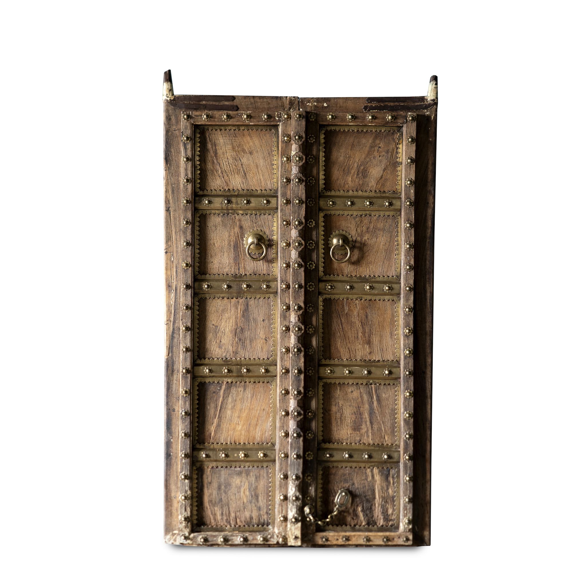White background image of an antique Indian temple door made of old teak with original brass fittings, locks, and ring handles, featuring a richly aged patina from a historic Jain temple.