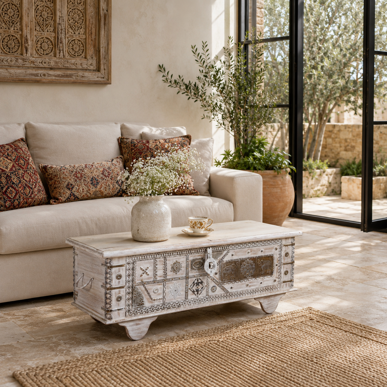 Lifestyle image of a Janash whitewashed mango wood coffee table chest with decorative iron fittings and wooden wheels 116cm