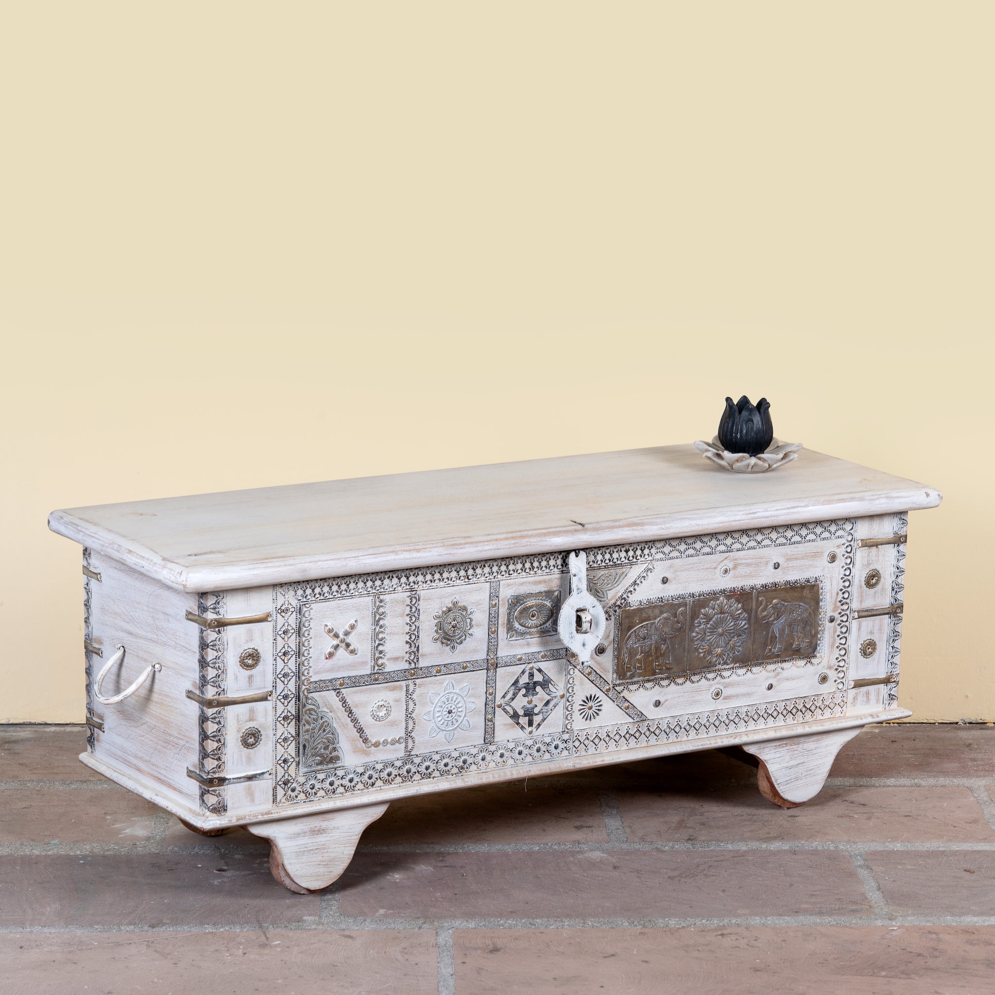 Side angle image of a Janash whitewashed mango wood coffee table chest with decorative iron fittings and wooden wheels 116cm