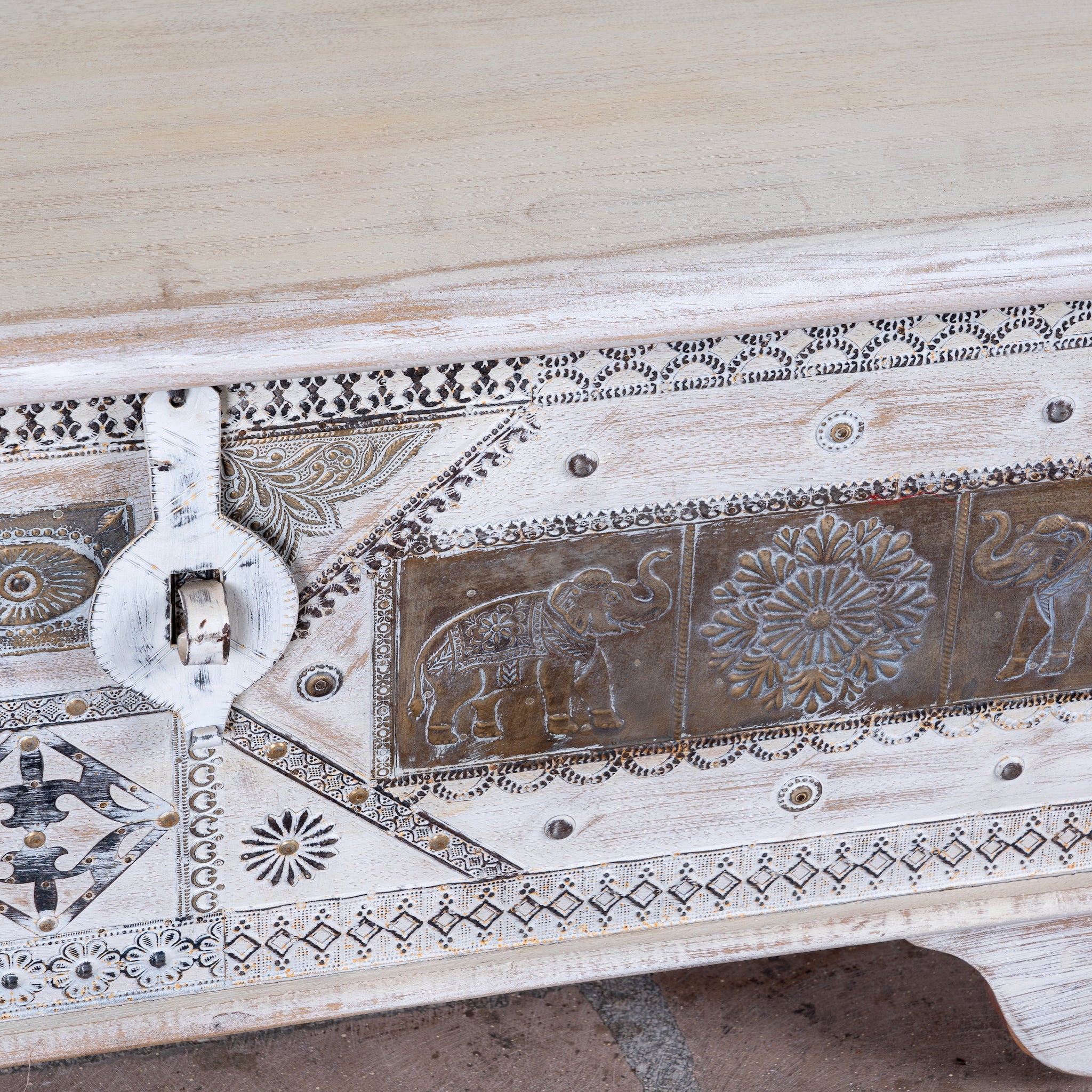Close up image of a Janash whitewashed mango wood coffee table chest with decorative iron fittings and wooden wheels 116cm