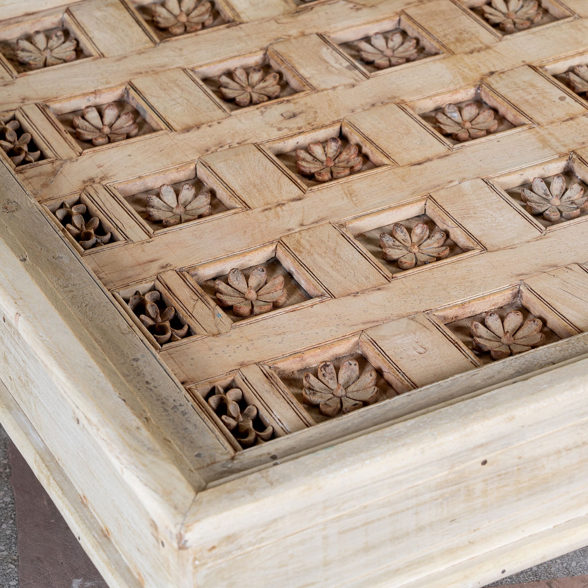 Close up image of a Jayson reclaimed teak wood coffee table with glass top, removable legs, and hand carved antique Indian ceiling panel.