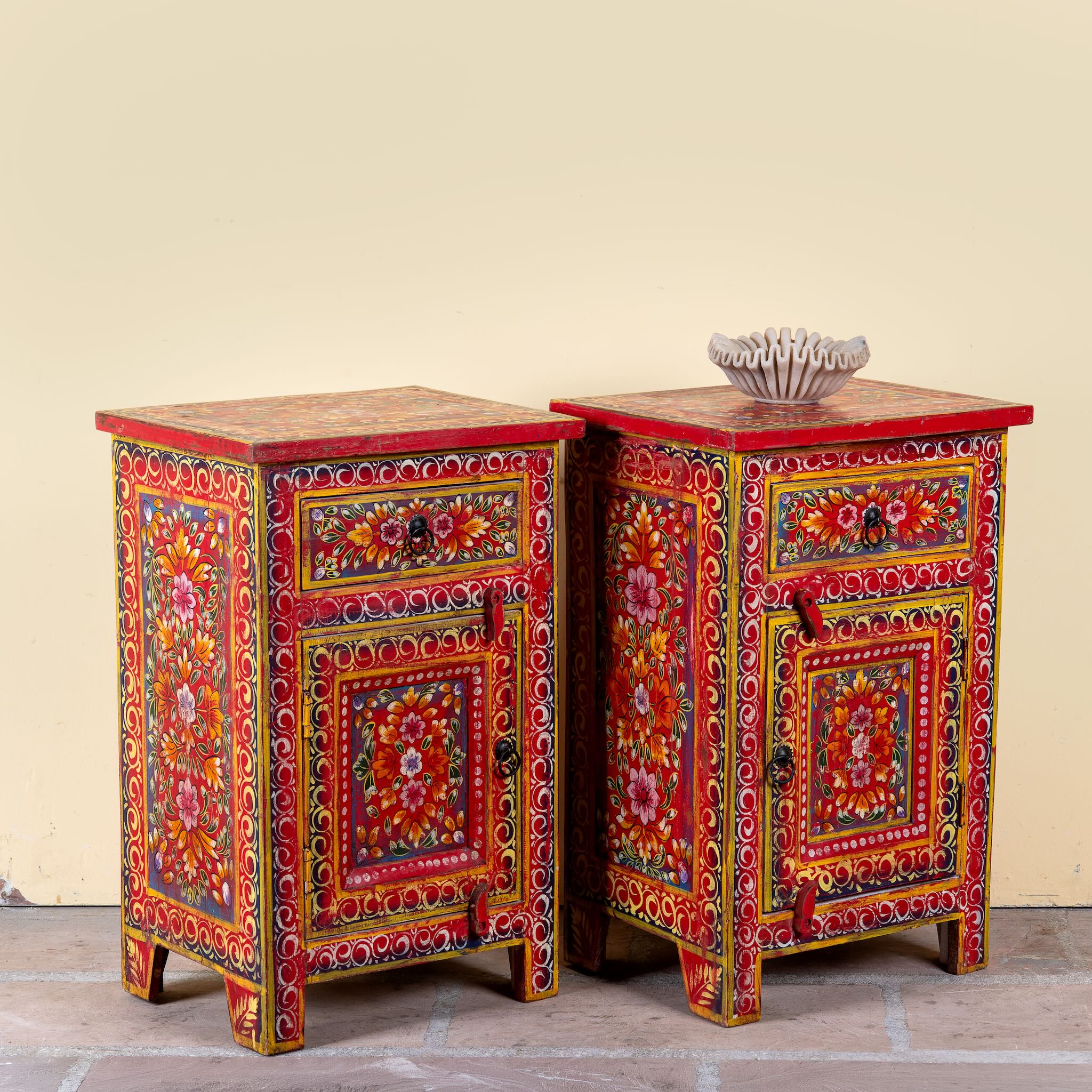 Side angle image of a Joven pair of hand painted reclaimed wood nightstands with one drawer, one cabinet door, floral artwork, and vibrant red boho style finish.