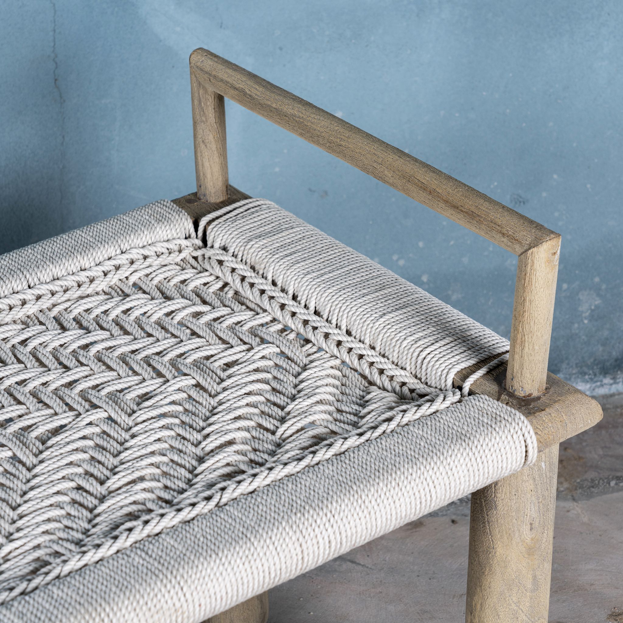 Close up of a Japandi style wooden bench with hand woven seating in a mediterrane scene.