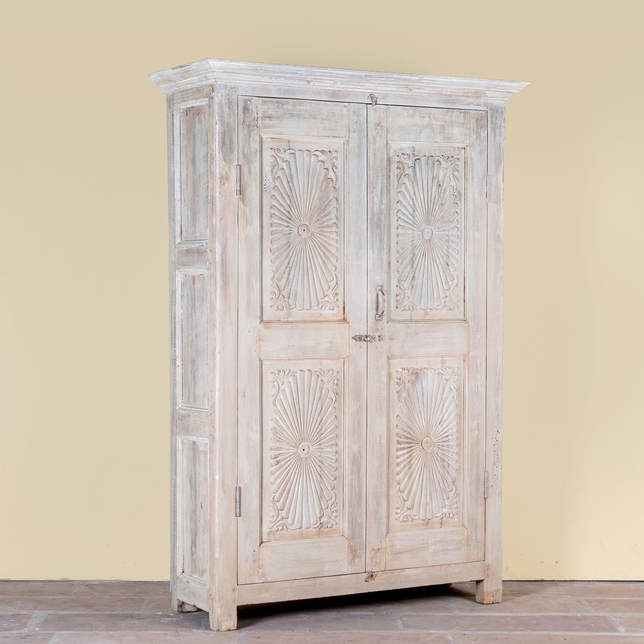 Side angle image of a Kaiden reclaimed teak wood wardrobe with hand-carved Indian details, double doors, and vintage whitewashed finish.