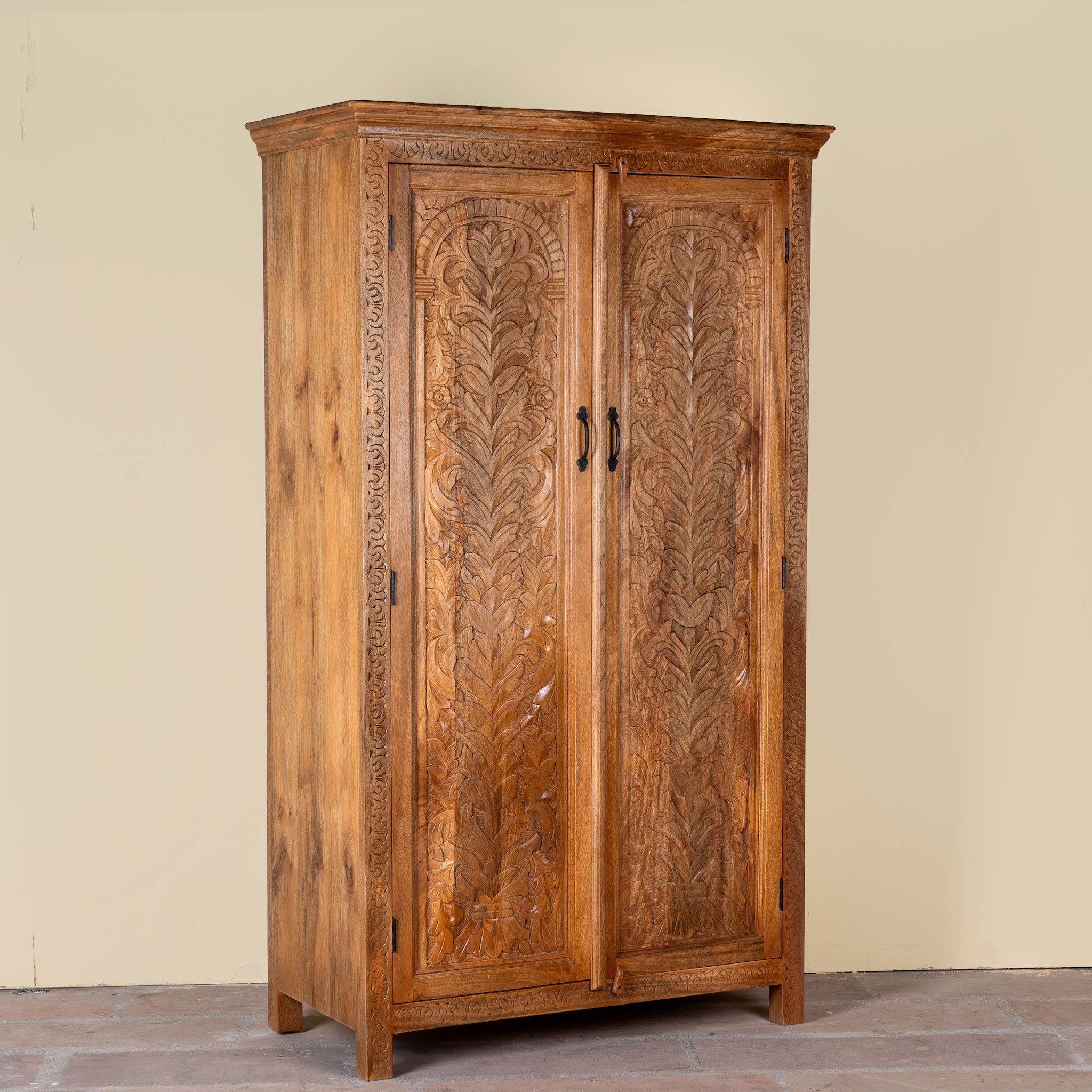 Side angle image of a Kalki hand carved mango wood wardrobe with botanical carved doors, removable shelves and hanging rail, 110x56x190cm
