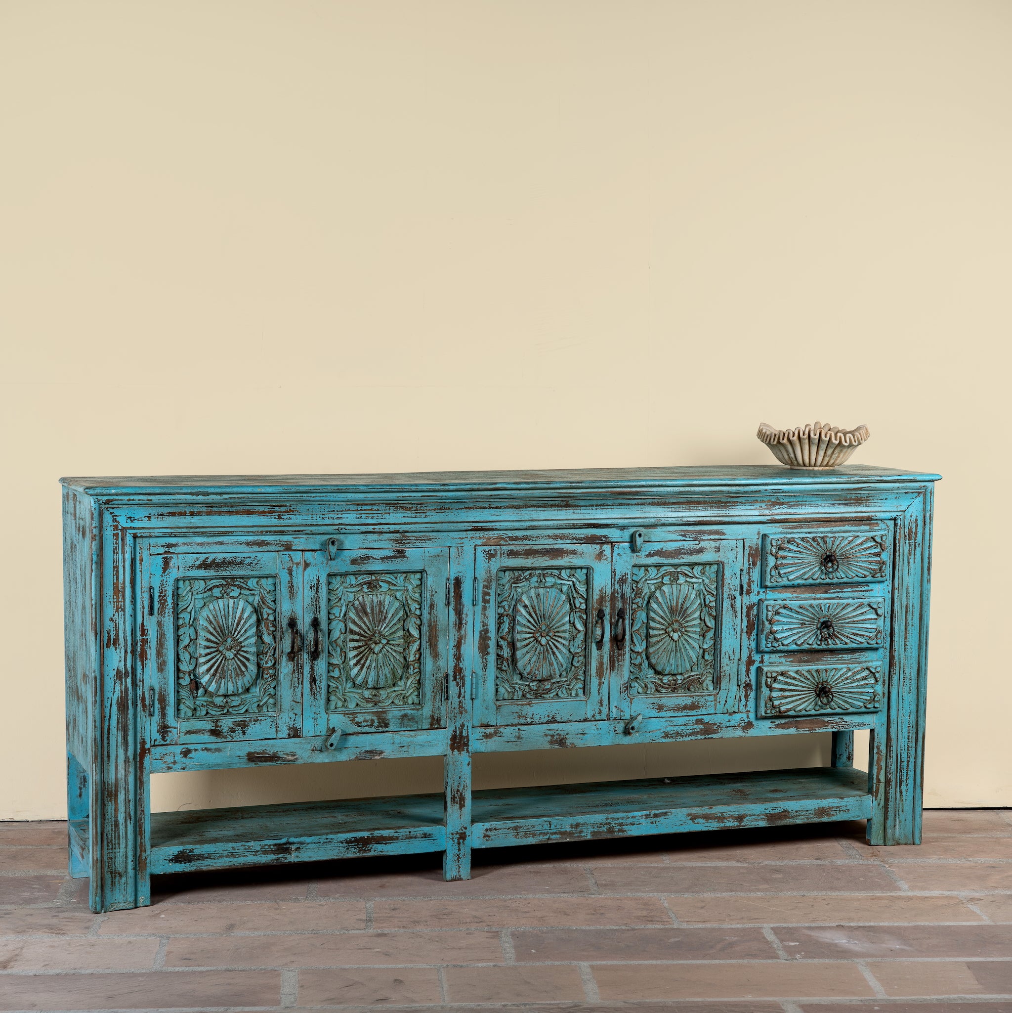 Side angle image of a Kalpana reclaimed wood console table with blue distressed finish, carved doors, three drawers, enclosed storage and open lower shelf.