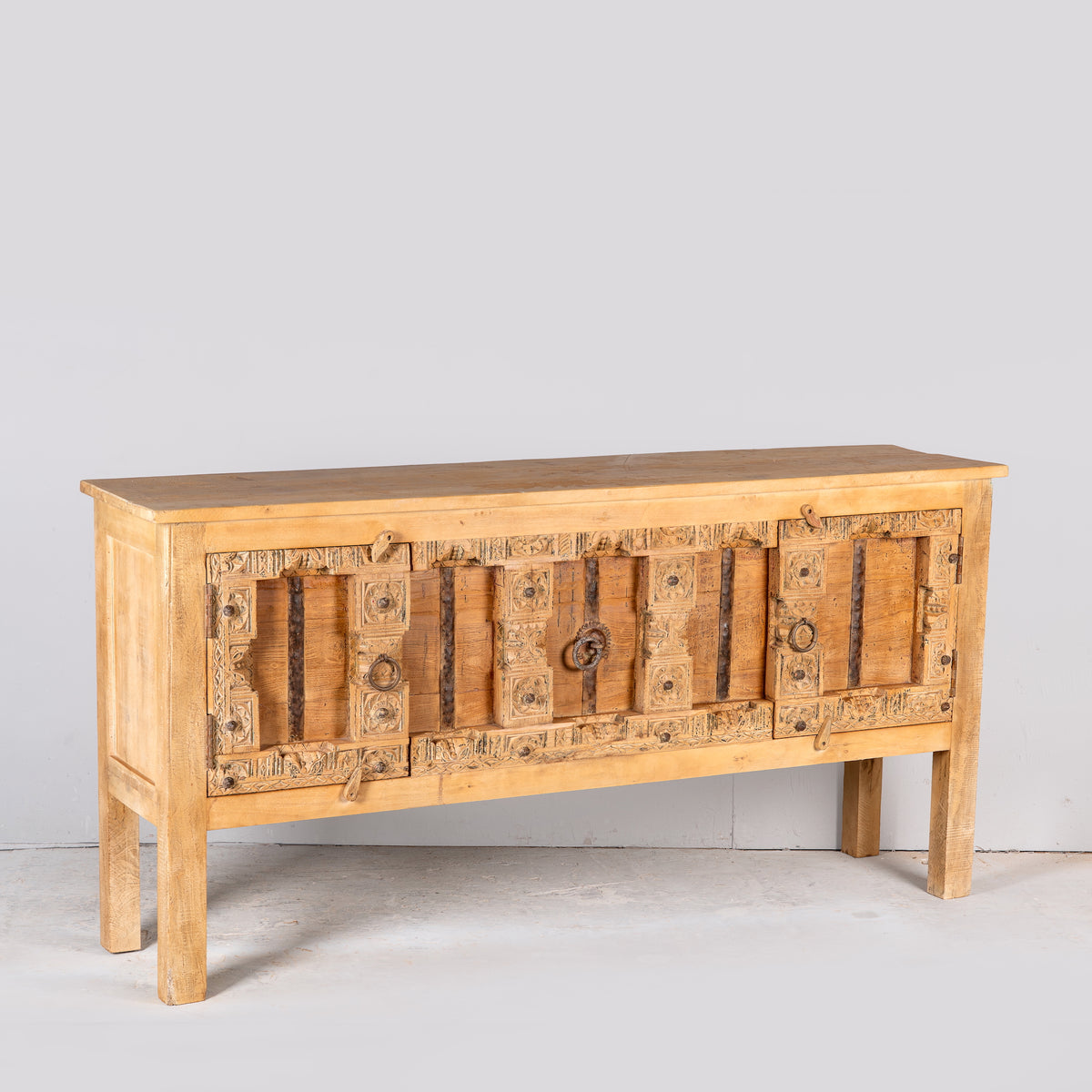 Side angle image of a Kanan console table made from old teak door panels, featuring traditional hand-carved details, iron ring accents, and built-in storage in a natural rustic finish.