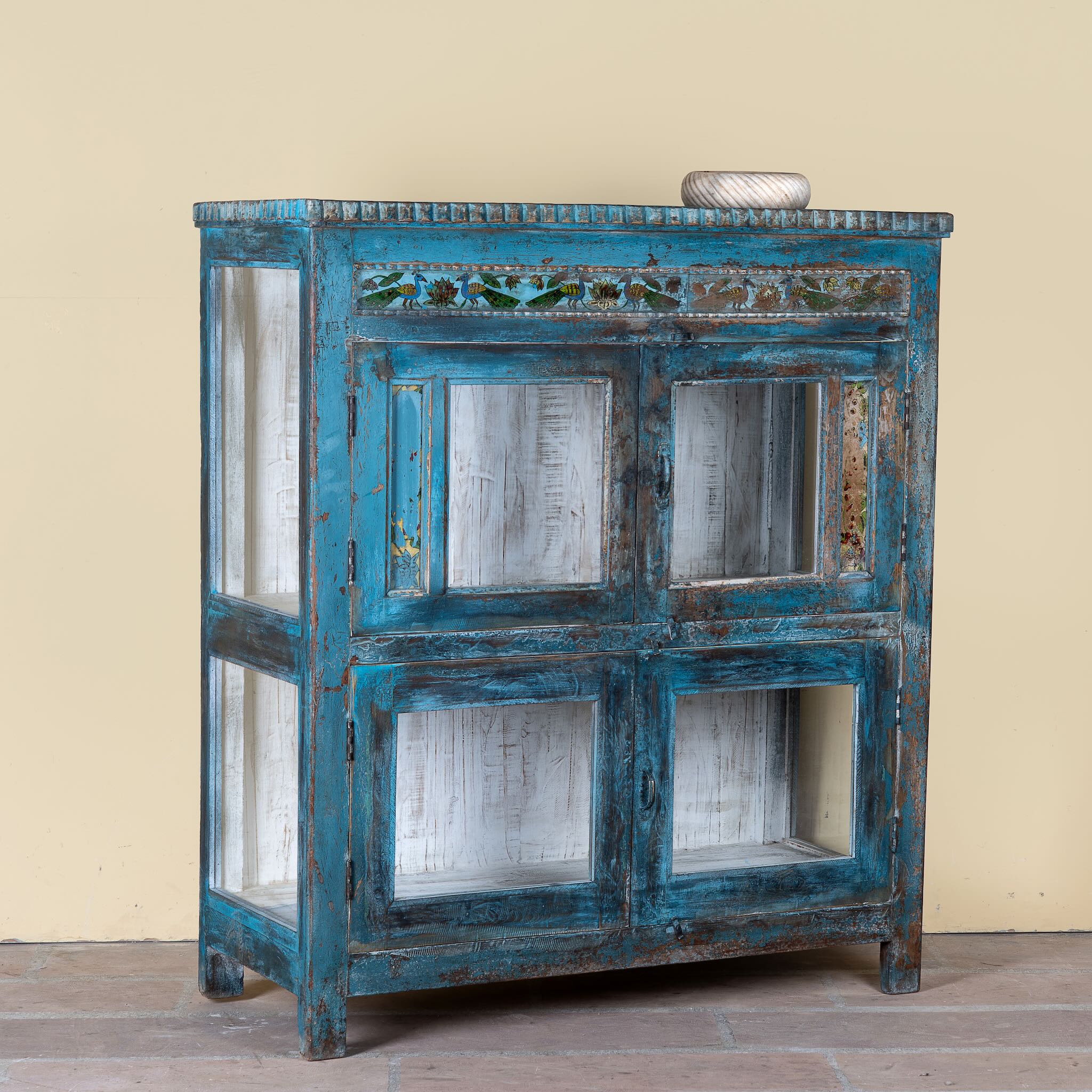 Side angle image of a Kavish vintage blue reclaimed teak wood wardrobe with peacock reverse glass paintings and distressed Indian finish.