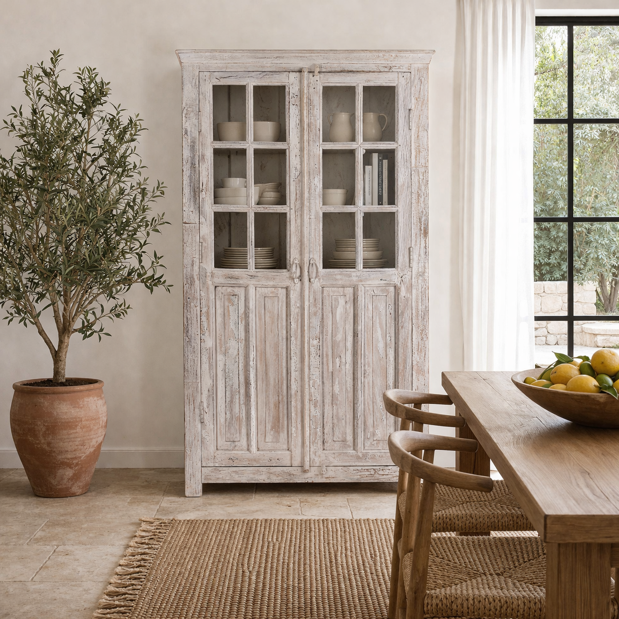 Lifestyle image of a refurbished antique teak wood display cabinet with whitewashed finish and glass doors – wooden display cabinet blending Mediterranean charm and timeless craftsmanship.