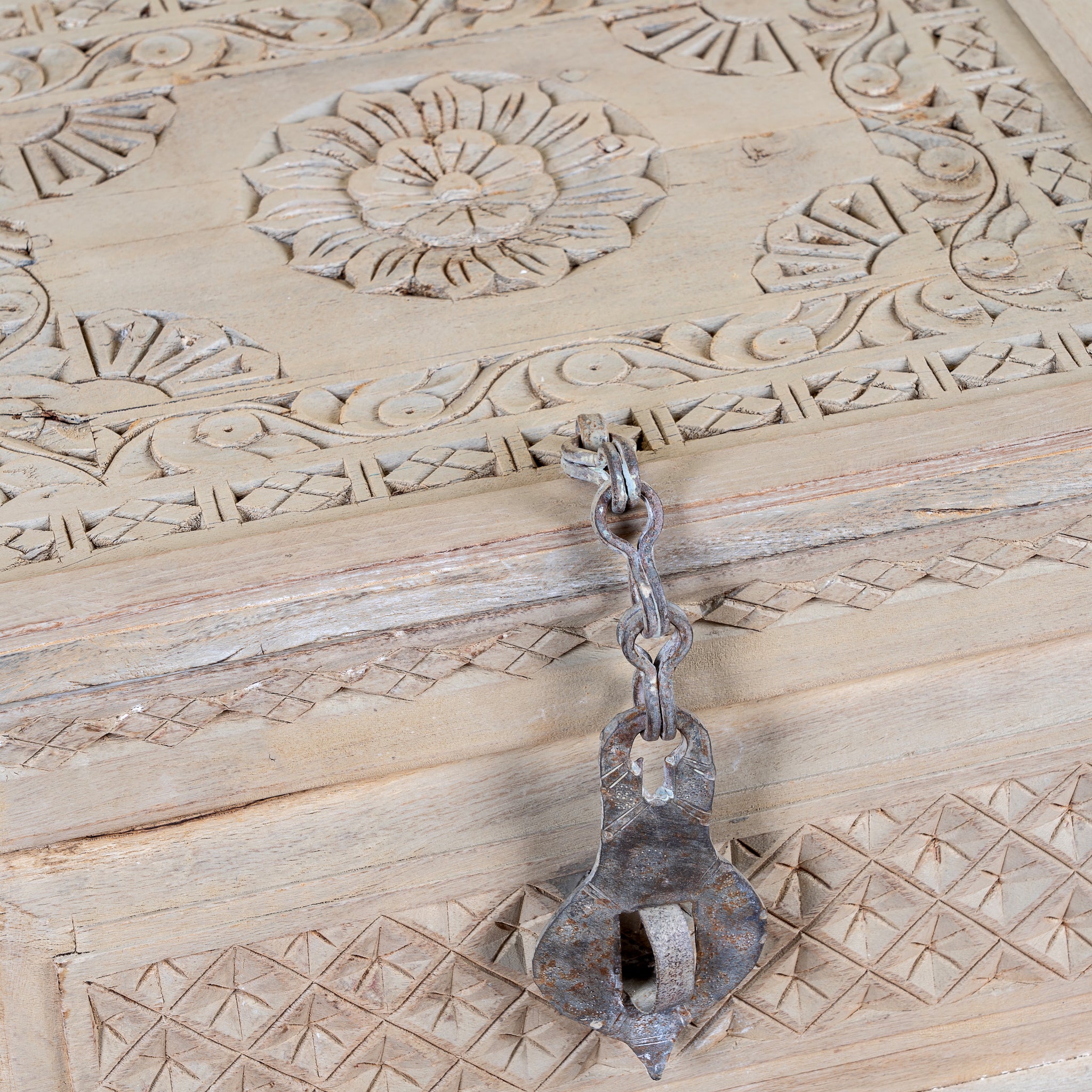 A rustic, antique-style metal latch with a chain lock resting on a carved wooden box lid.