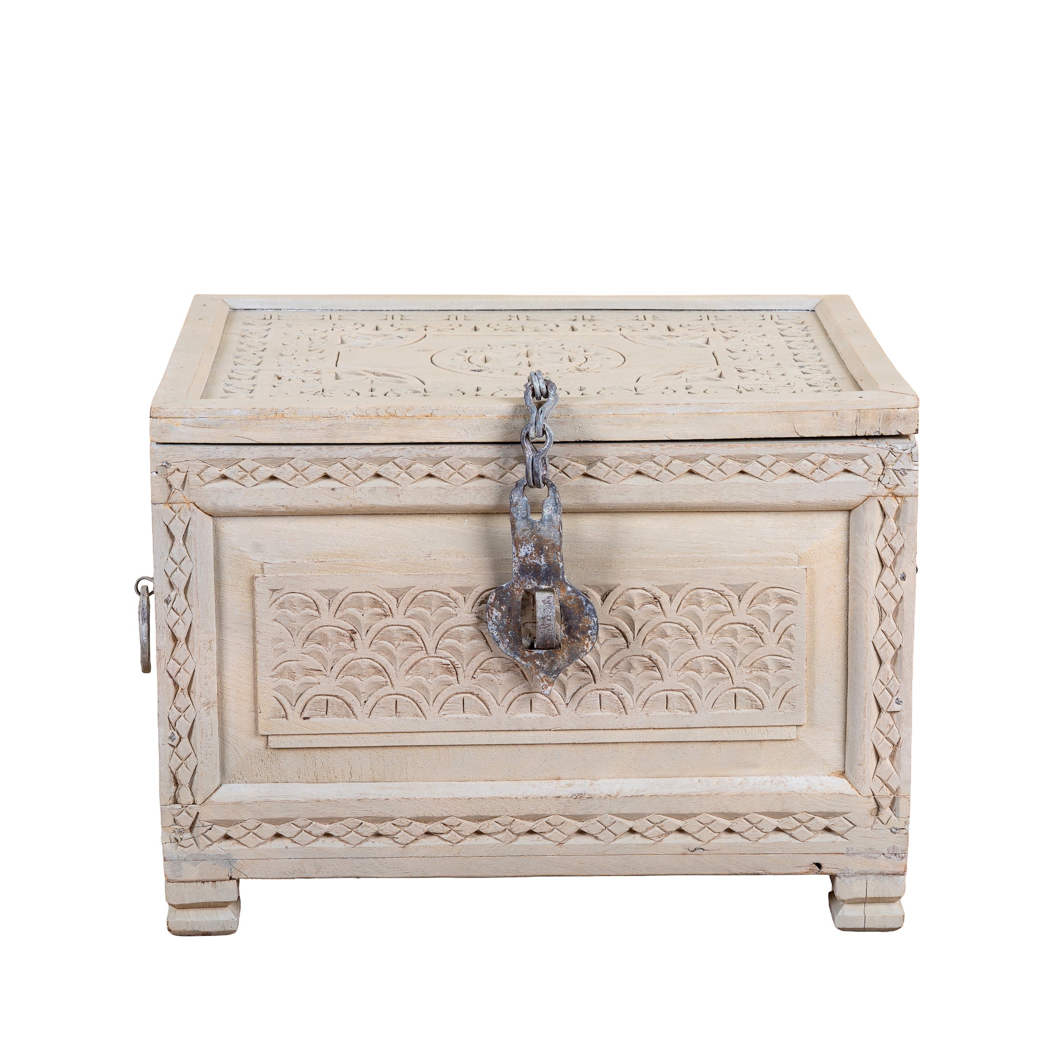 A rectangular carved wooden chest with a distressed off-white finish, featuring intricate geometric and floral engravings on the lid and front panel, a rustic metal latch with a chain, and small feet at the bottom, shown on a plain white background.