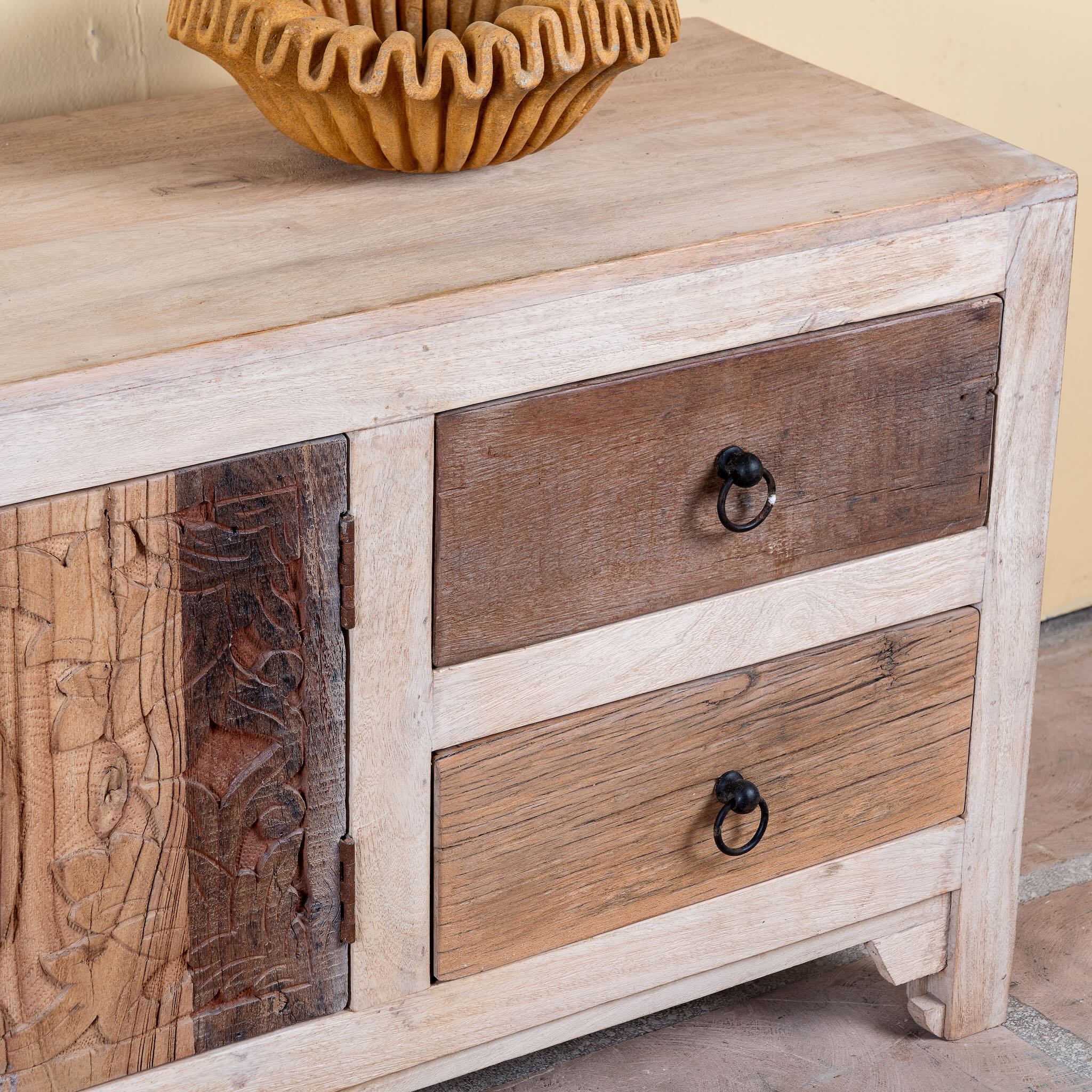 Close up image of a Kishen handcrafted reclaimed wood lowboard with driftwood front detailing, carved cabinet doors, four drawers, and natural rustic boho style finish.