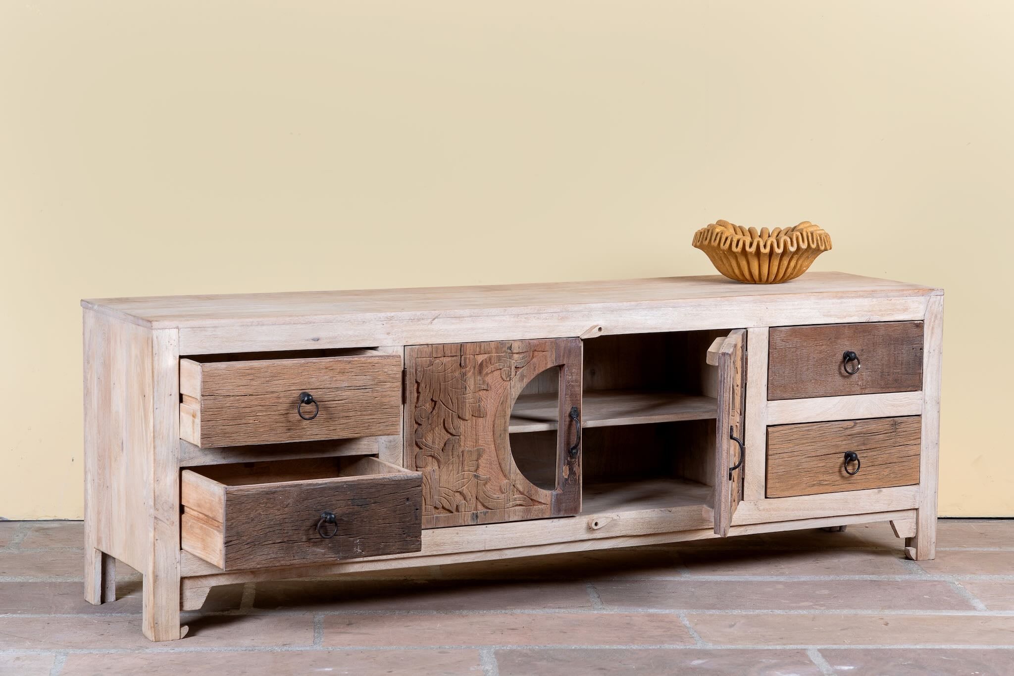 Side angle image with open doors of a Kishen handcrafted reclaimed wood lowboard with driftwood front detailing, carved cabinet doors, four drawers, and natural rustic boho style finish.