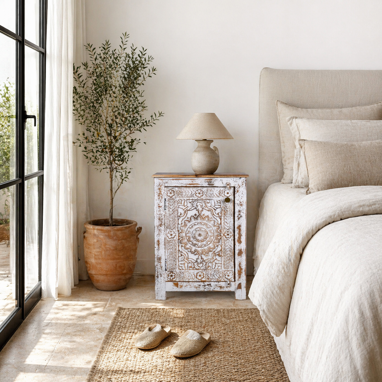 Lifestyle image of a hand carved bedside table with mandala and floral motifs; reclaimed wood in white washed furniture style, 50 × 40 × 72 cm.
