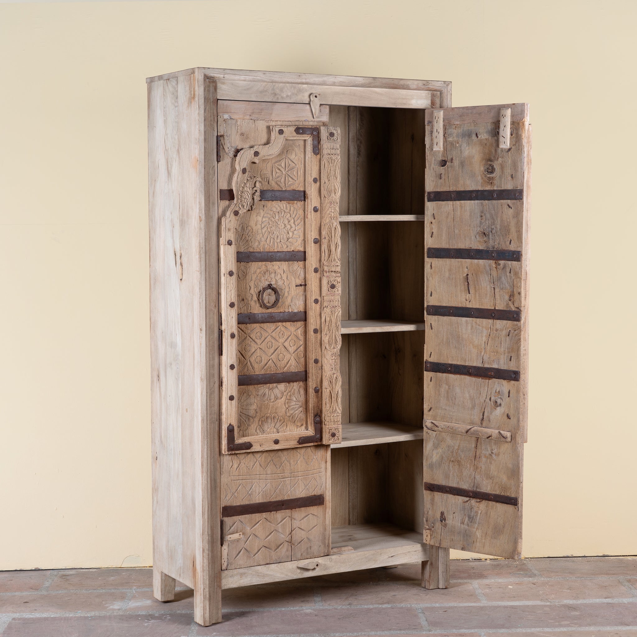 Side angle image with open doors of a Lakshya bleached mango wood cabinet with original hand carved Indian door panels and iron fittings 167cm