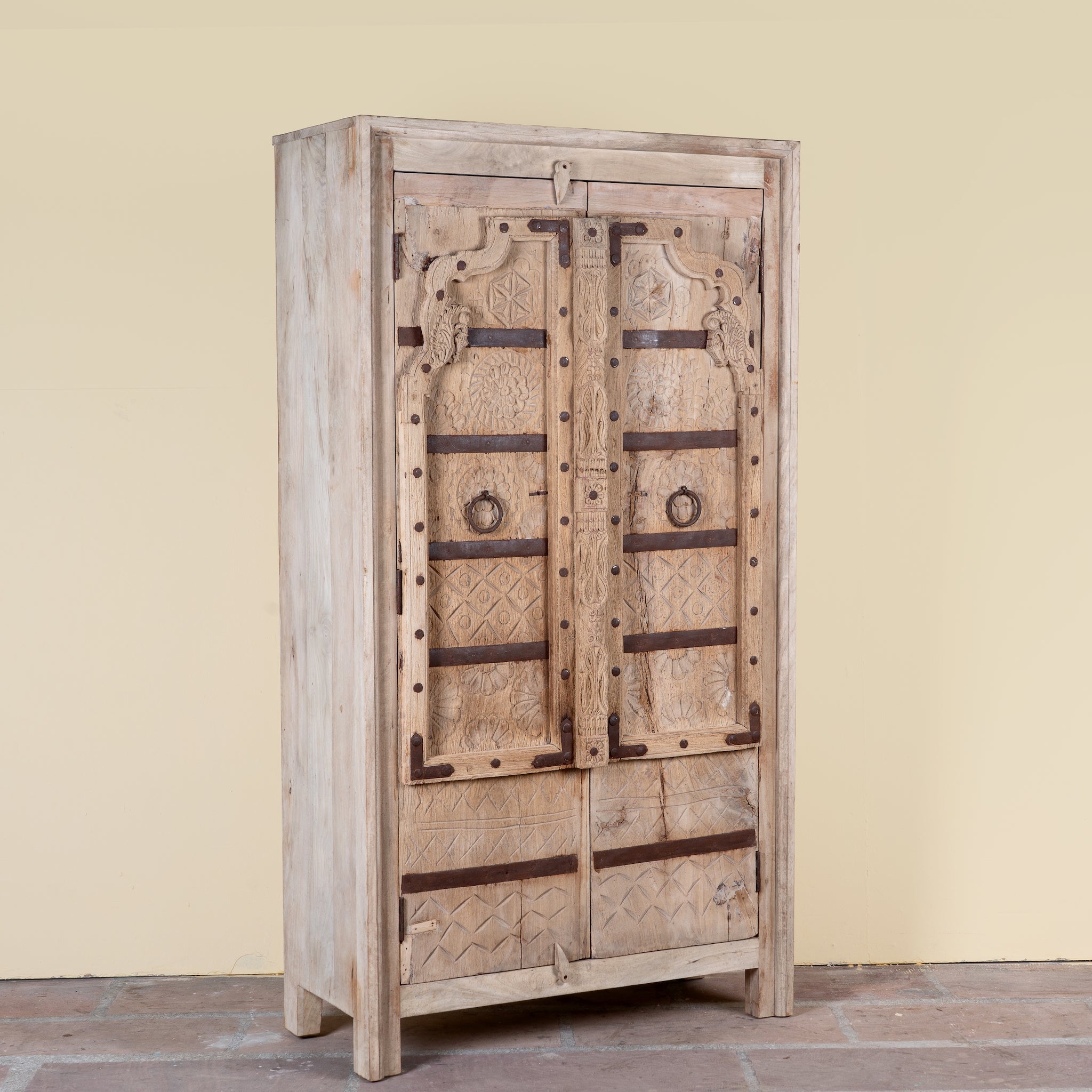 Side angle image of a Lakshya bleached mango wood cabinet with original hand carved Indian door panels and iron fittings 167cm
