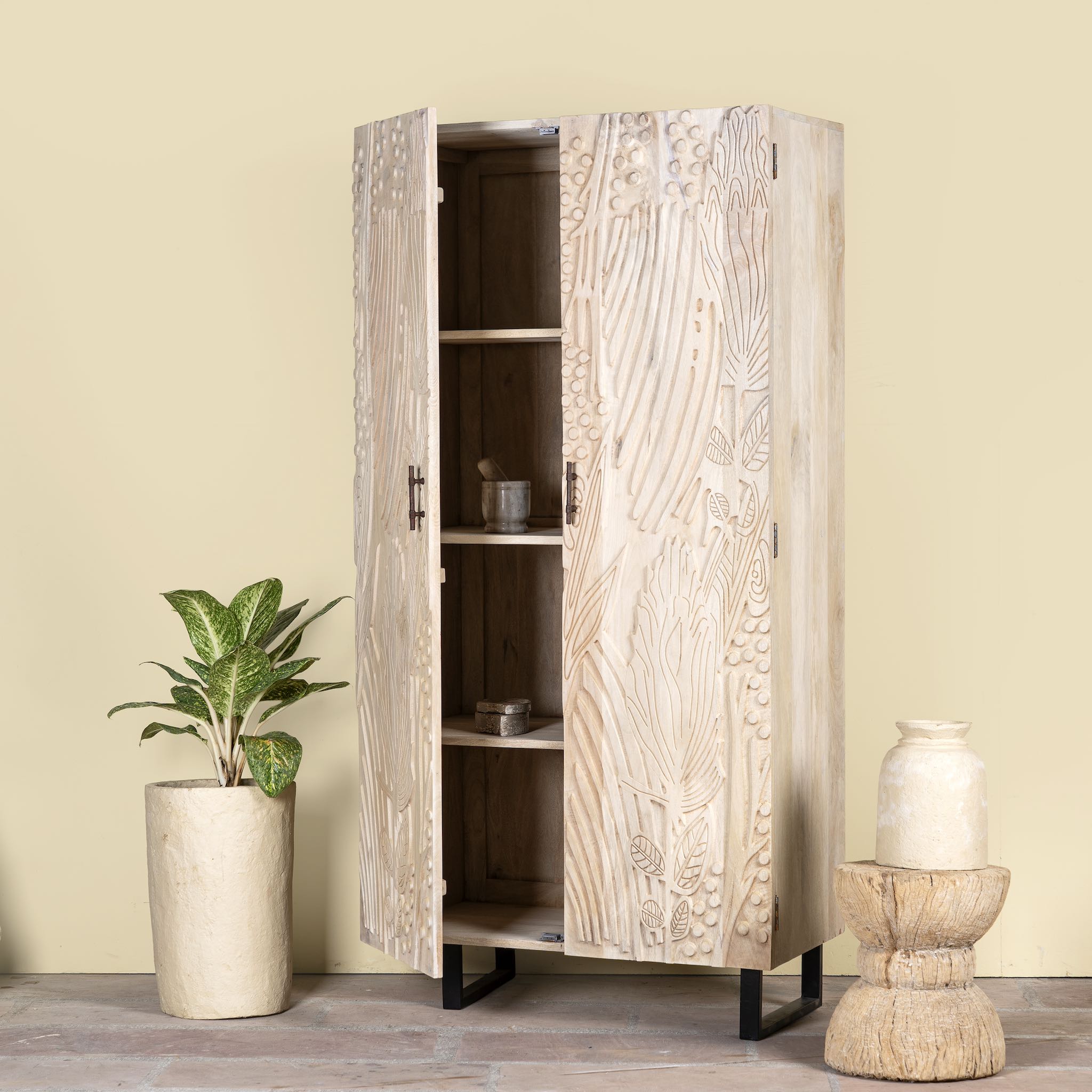 Side angle image with open door of a mango wood wardrobe with sandblasted finish and iron stand; artisanal bedroom furniture, 90 × 46 × 183 cm.