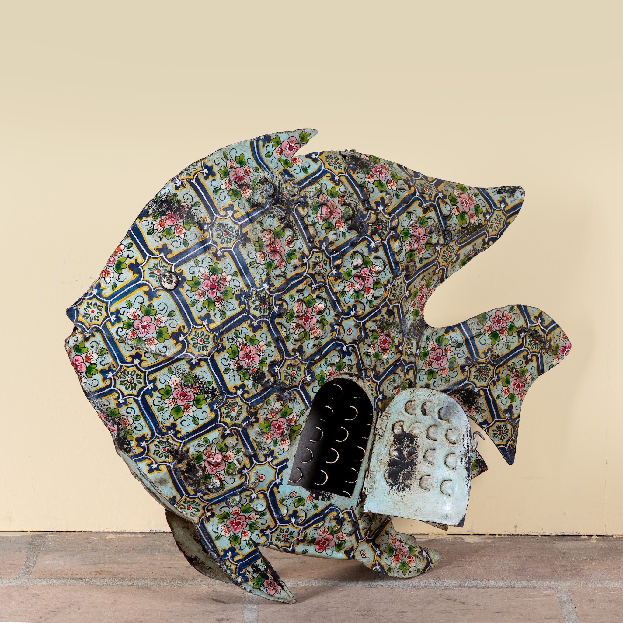 Side angle image of a Maah hand painted freestanding metal fish sculpture featuring Delft-inspired blue tile patterns with pink floral motifs, handcrafted decorative home accessory, 107x15x80cm.
