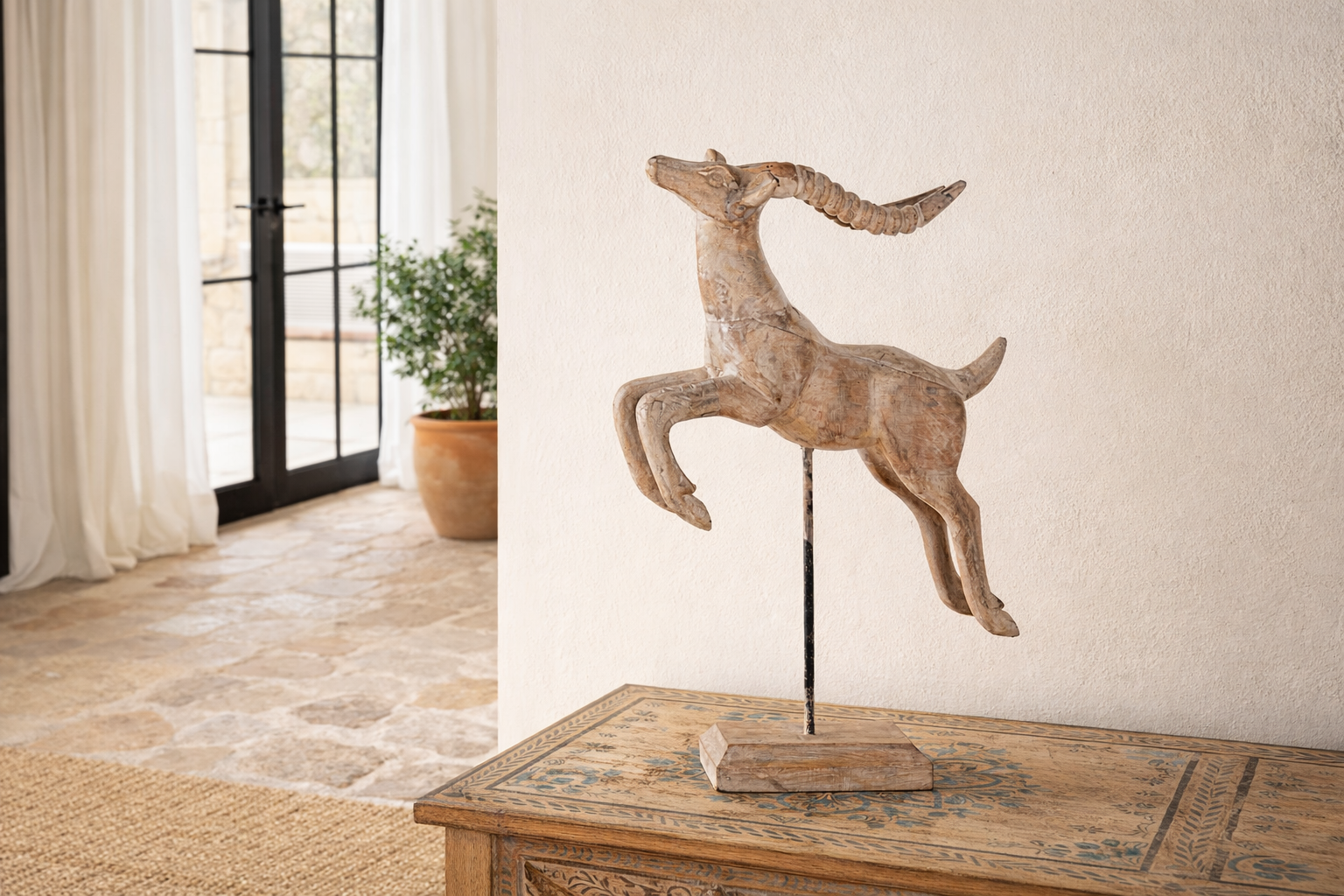 Lifestyle image of a handcrafted wooden deer sculpture Rijul on an iron stand with a whitewashed finish. A vintage home accessory and unique Indian decoration ideal for vintage home decor on consoles or shelves.