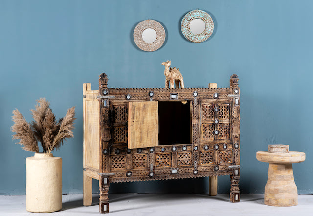 Side angle image with open door of an antique Indian treasure chest in solid teak with sandblasted finish, hand-carved details, and iron accents. Vintage home accessory for eclectic Indian decor, 127 × 110 × 47 cm.