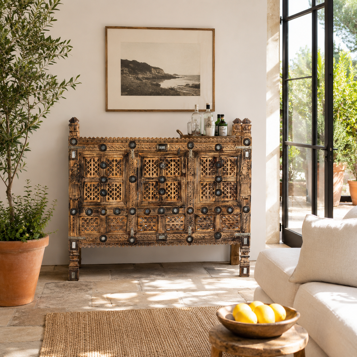 Lifestyle image of an antique Indian treasure chest in solid teak with sandblasted finish, hand-carved details, and iron accents. Vintage home accessory for eclectic Indian decor, 127 × 110 × 47 cm.