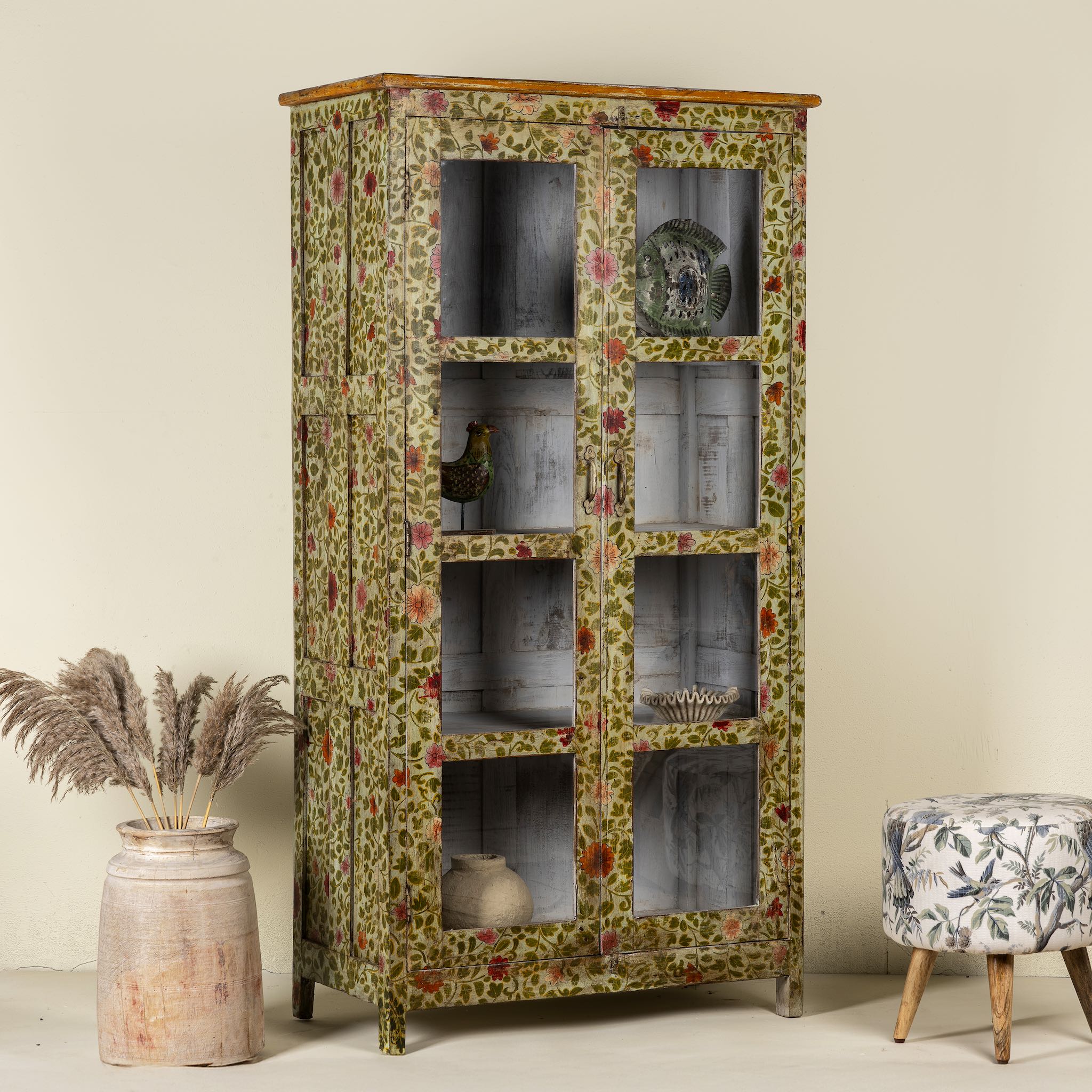 Side angle image of a hand-painted reclaimed wood cabinet with glass doors and floral motifs – sustainable and artistic furniture for vintage or bohemian interiors.