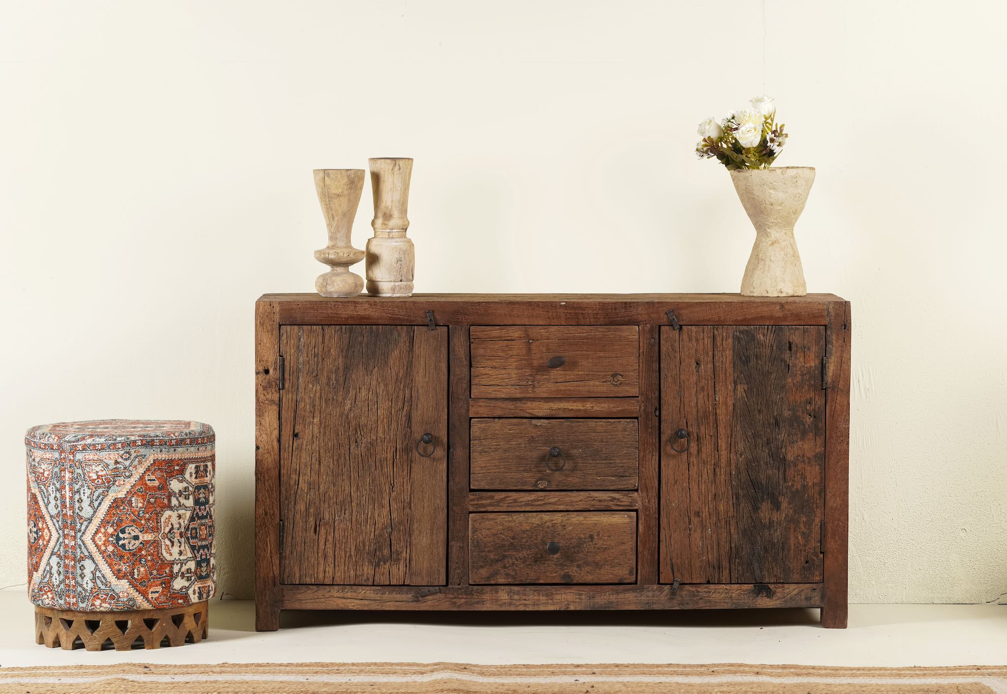 A rustic wooden sideboard Naresh with two cabinets and three drawers, alongside a decorative vase and a small plant on top, set against a neutral background.